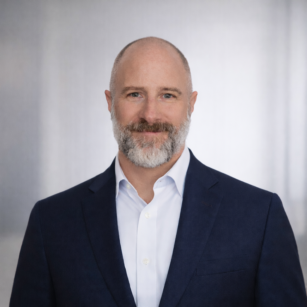 A middle-aged man with a beard and bald head wearing a navy blazer and white dress shirt, smiling at the camera.