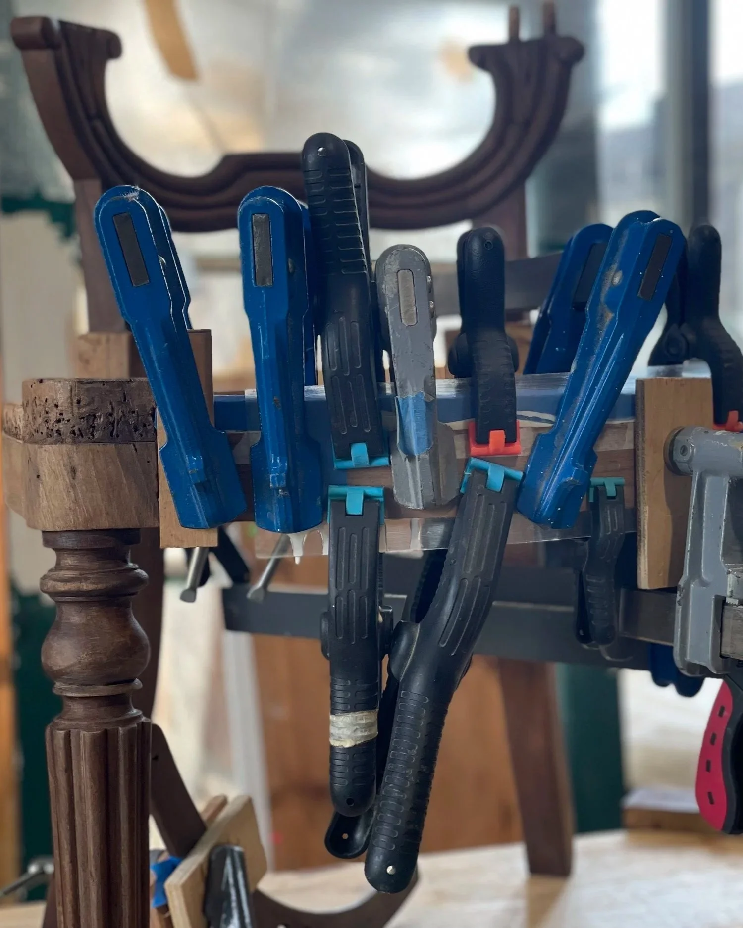 Une collection de serre-joints de différentes tailles suspendus à une étagère en bois dans un atelier. En arrière-plan, une partie d'un meuble en bois.