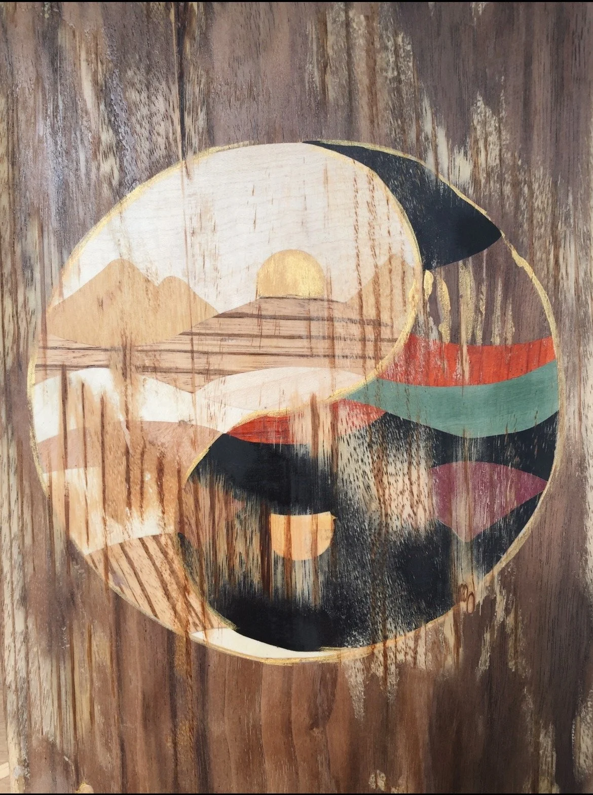 Table en bois avec une assiette en céramique de forme ovale contenant un paysage stylisé avec un soleil, des montagnes et un arbre, vu de dessus.