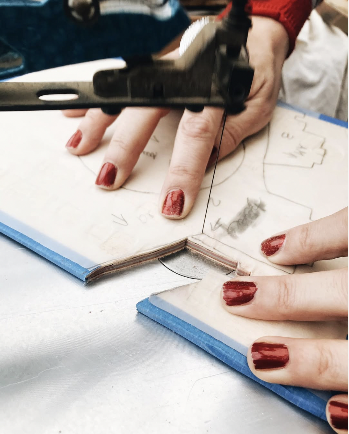 Une personne utilisant une scie pour couper un livre ou un panneau en bois, avec un croquis dessiné à la main sur la surface.