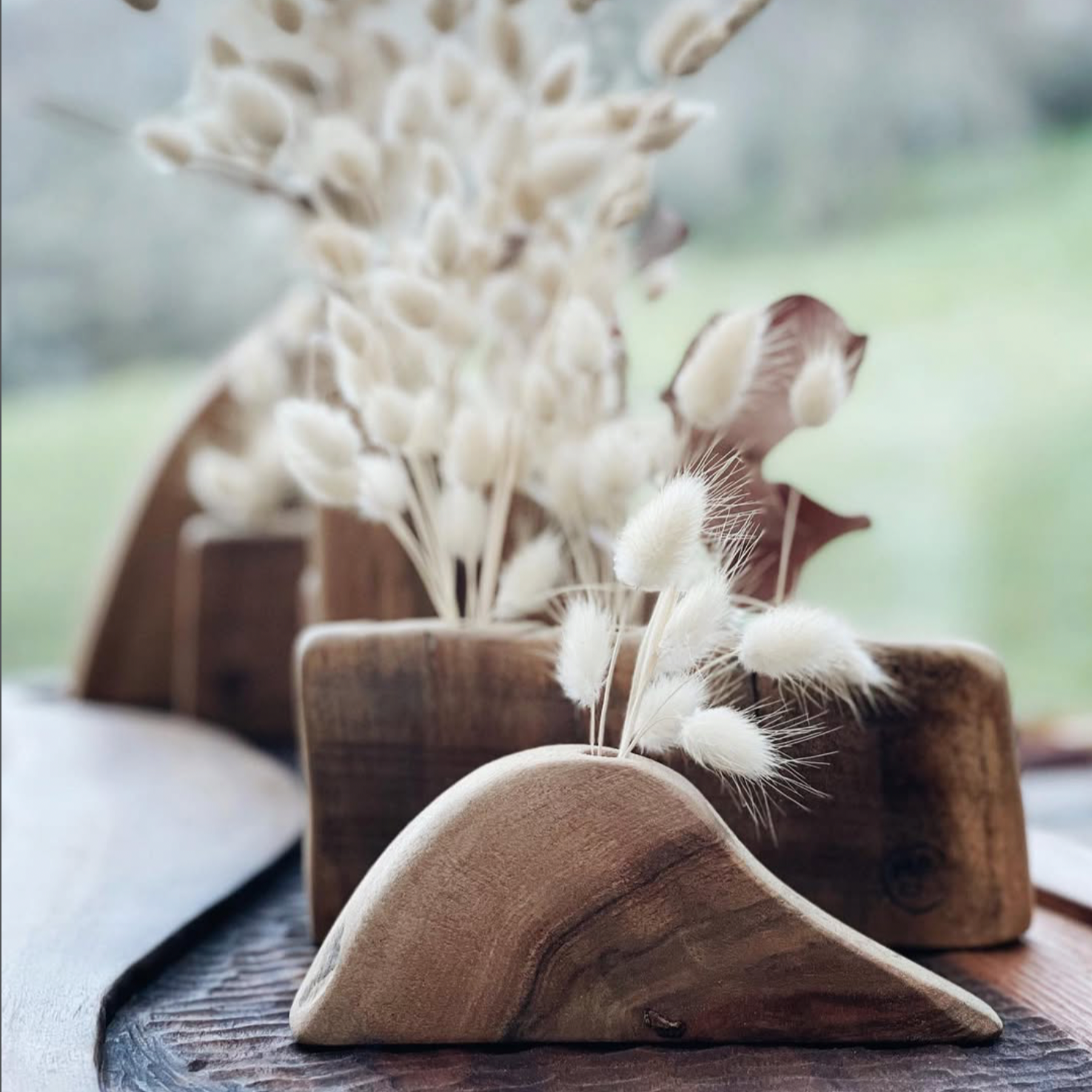 Arrangement de bouquets de fleurs en coton blanc dans des supports en bois sur une table en bois.