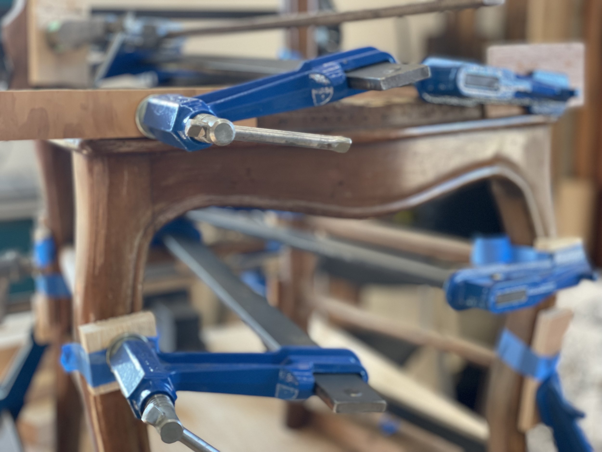 Pièce en bois d'une chaise ancienne en cours de restauration, fixée avec des serre-joints bleus.
