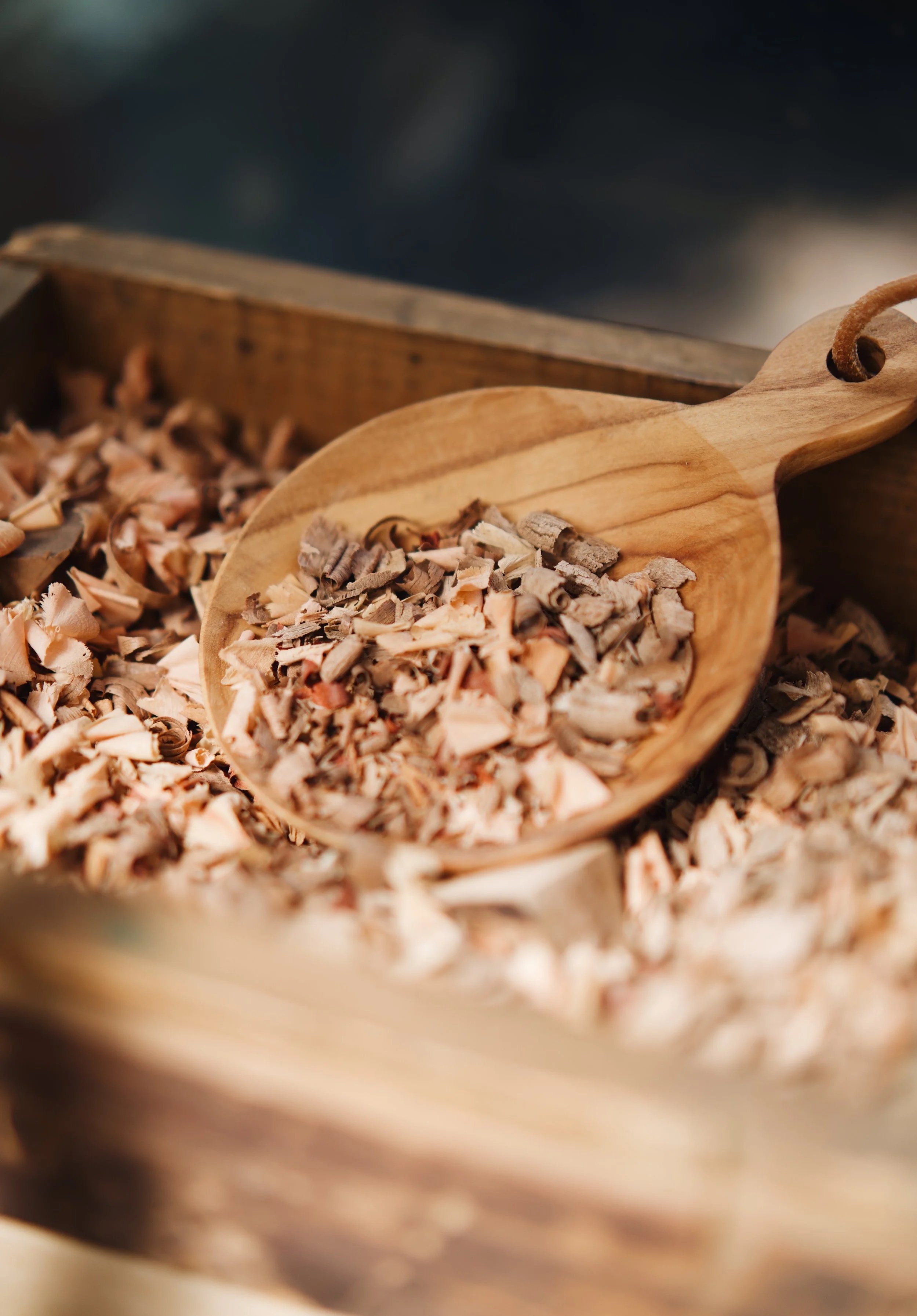 Petites écorces en bois dans une cuillère en bois, posées dans une caisse en bois.