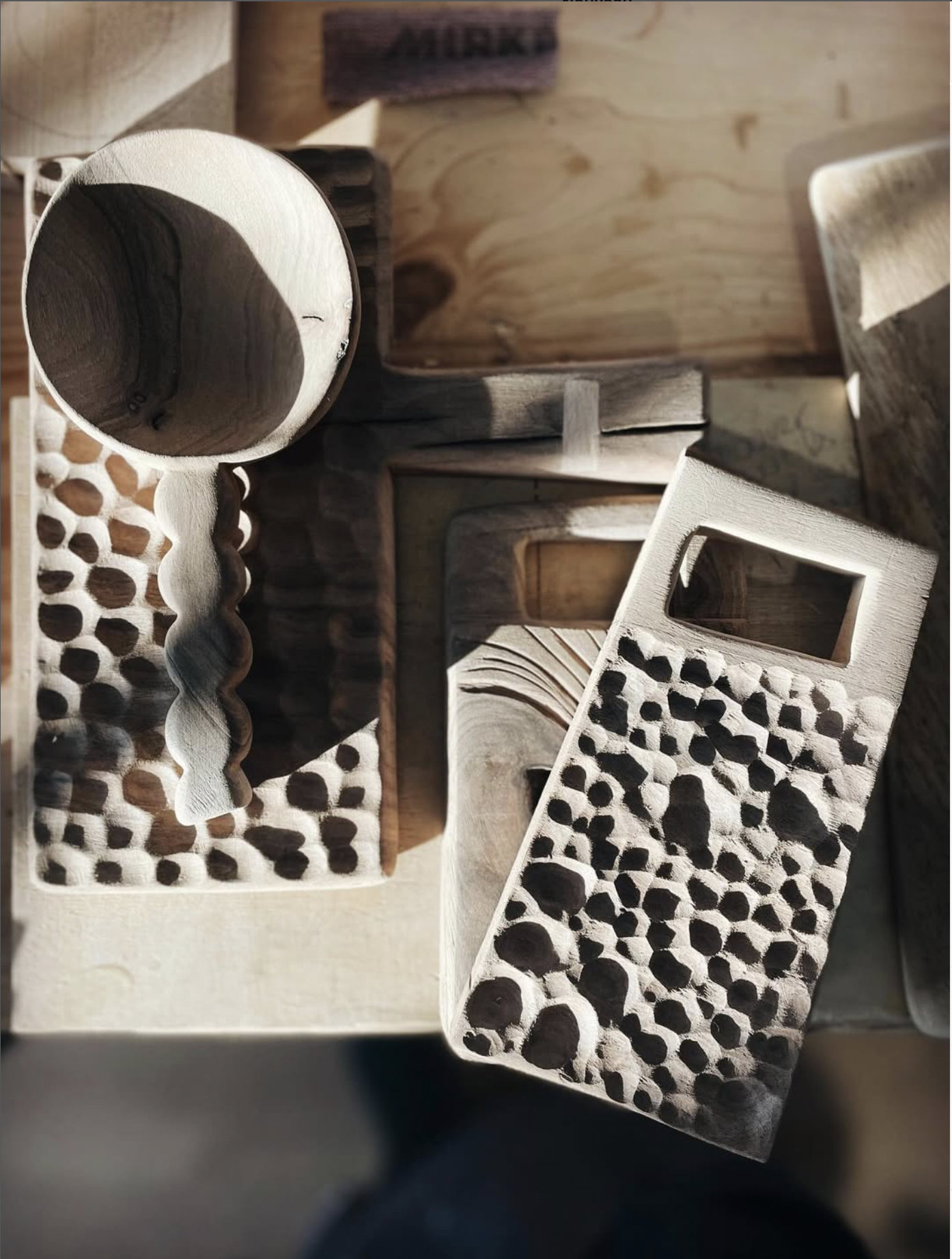 Divers objets en bois sculpté, dont un chapeau, une planche avec un motif de perforations, et plusieurs pièces en bois naturel, disposés sur une surface en bois.