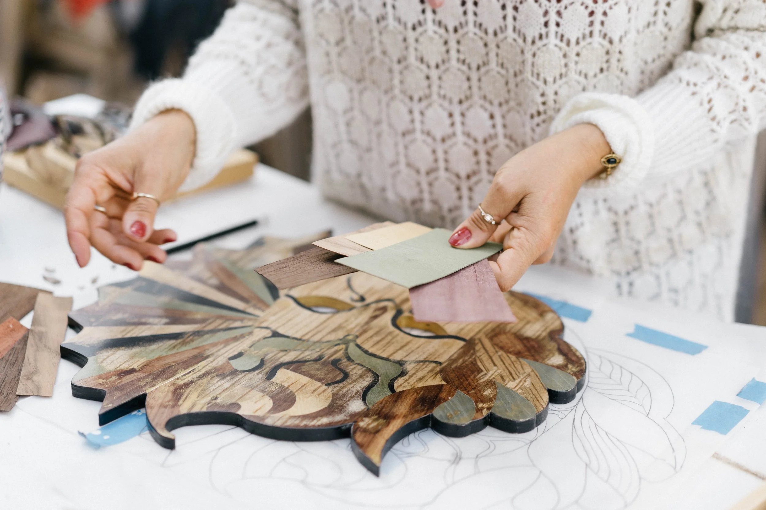 Une personne assise à une table, en train de sélectionner des petites pièces de bois colorées pour un projet de mosaïque ou d'art décoratif, posant sur un motif esquissé.