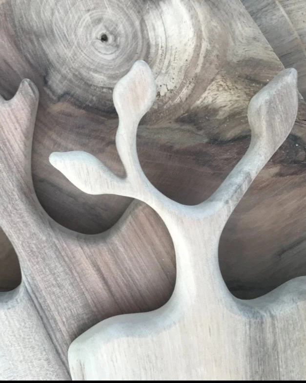 Une sculpture en bois représentant des formes d'arbres stylisées, avec des branches courbes et un grain visible dans le bois.