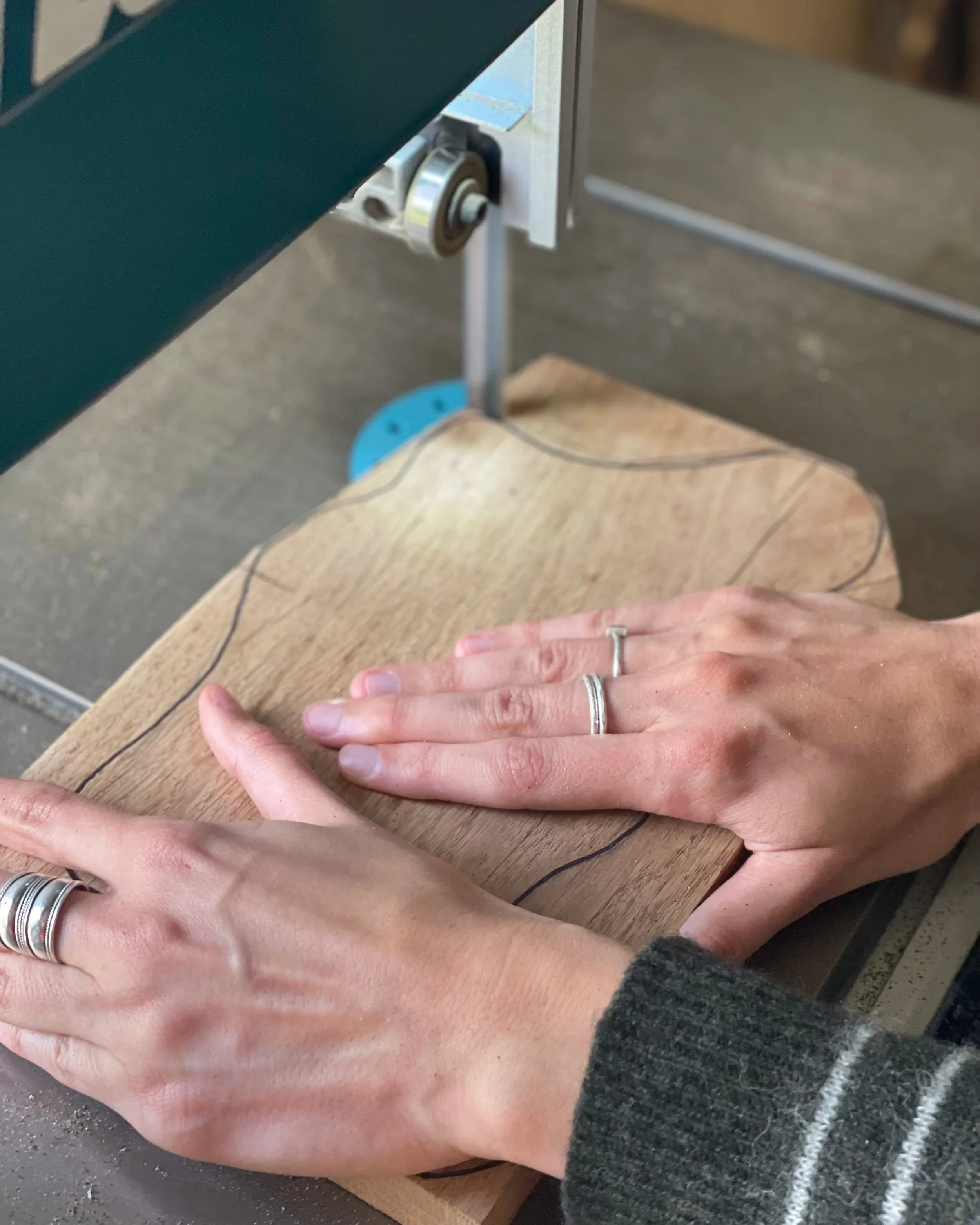 Deux mains positionnées sur une pièce de bois, probablement en train de la découper ou de la tracer, avec un outil de coupe électrique dans un atelier.