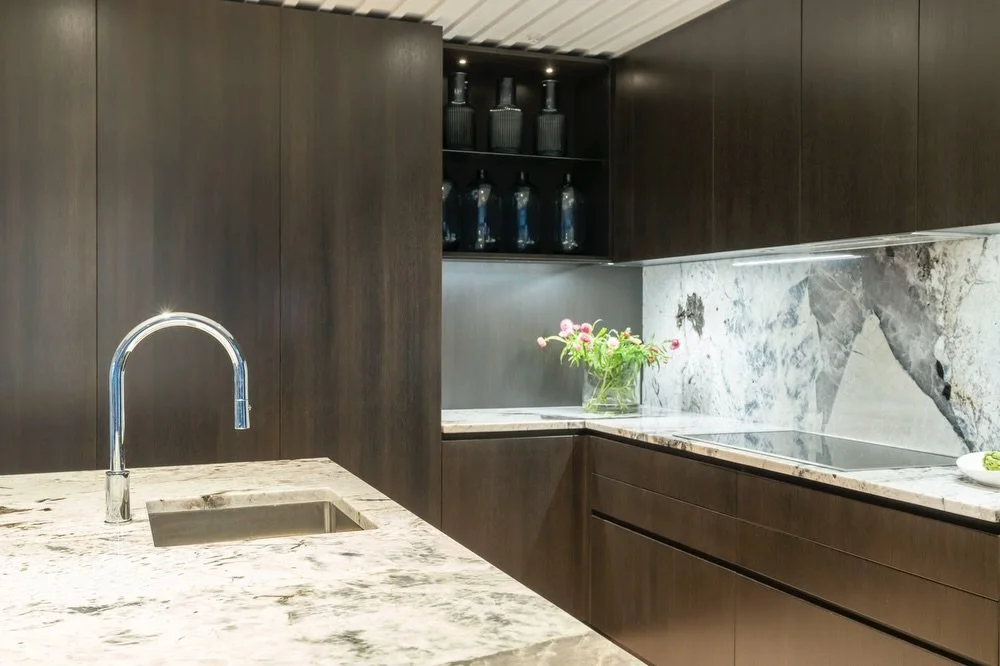 This kitchen brings crisp stone, textured timber detailing and a straight-through sightline tying into both the lounge and outdoor spaces.