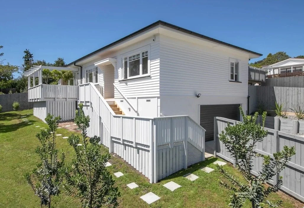 Exterior at our Titirangi renovation. The new double garage sits seamlessly beneath the lifted home, providing full internal access and a clean street presence.