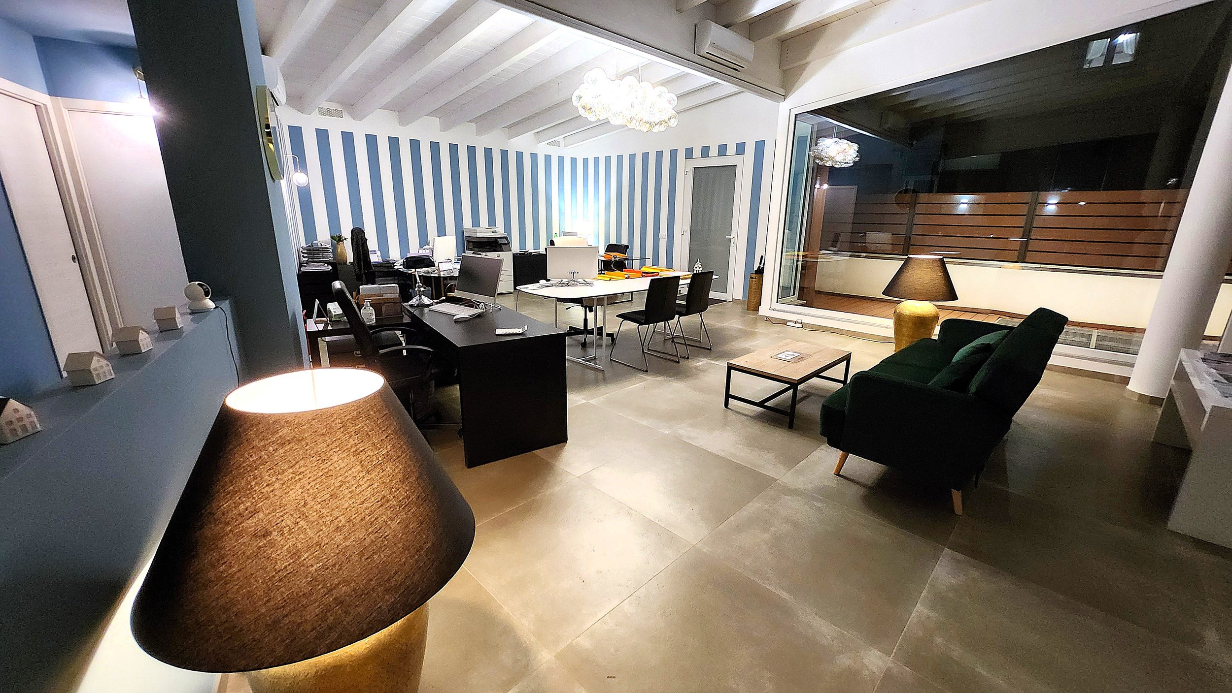 Ufficio con scrivanie, sedie e poltrona verde, lampade da tavolo e decorazioni