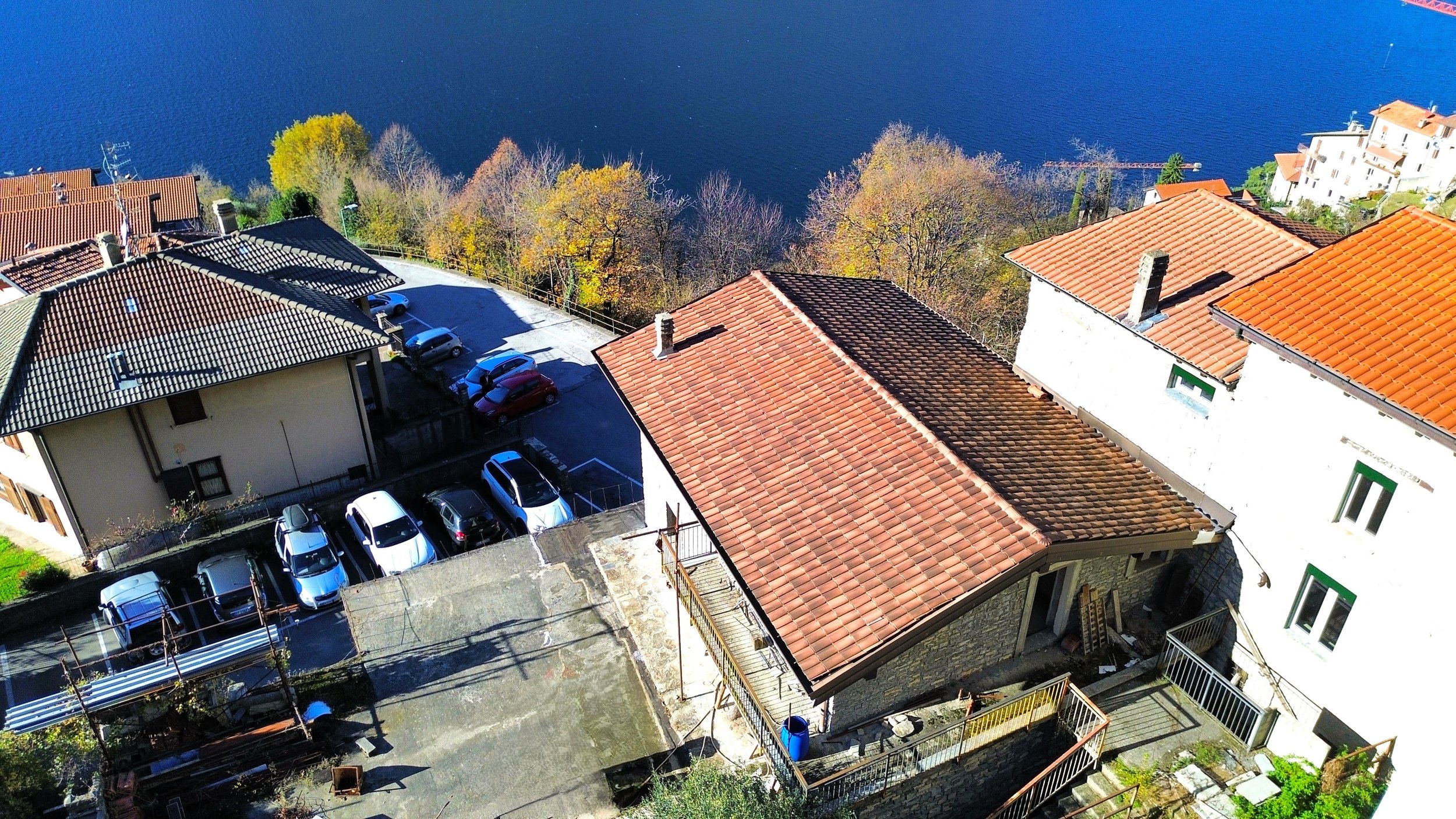 Foto aerea di un quartiere con case con tetti di tegole rosse, parcheggi e una vista su un lago con alberi autunnali.
