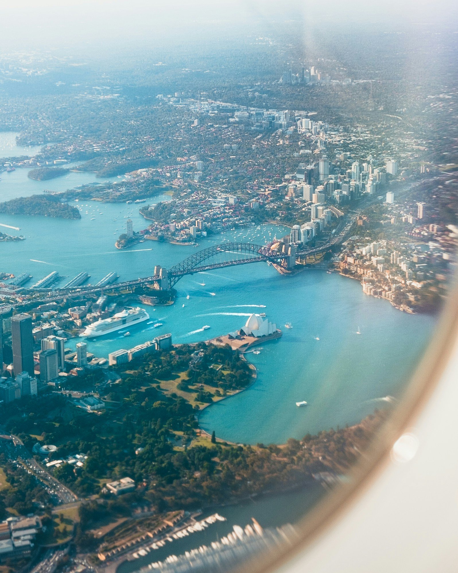 Aerial view of Sydney Harbour featuring the Sydney Opera House, Harbour Bridge, boats in the water, and city skyline.