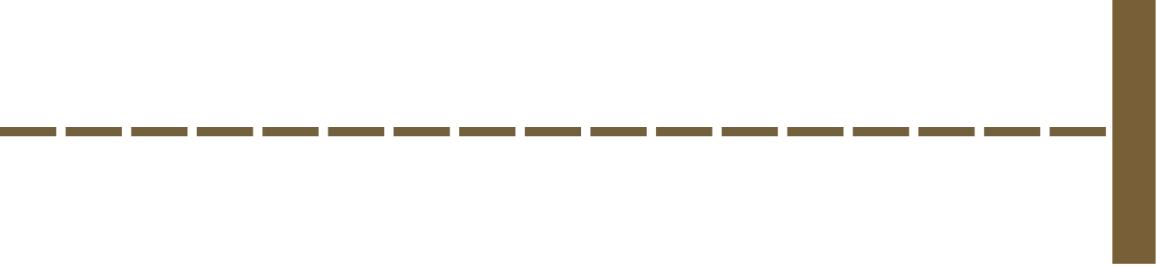 A close-up of a baseball or softball field, showing part of the infield dirt, the grass, and a brown outfield wall or fence.