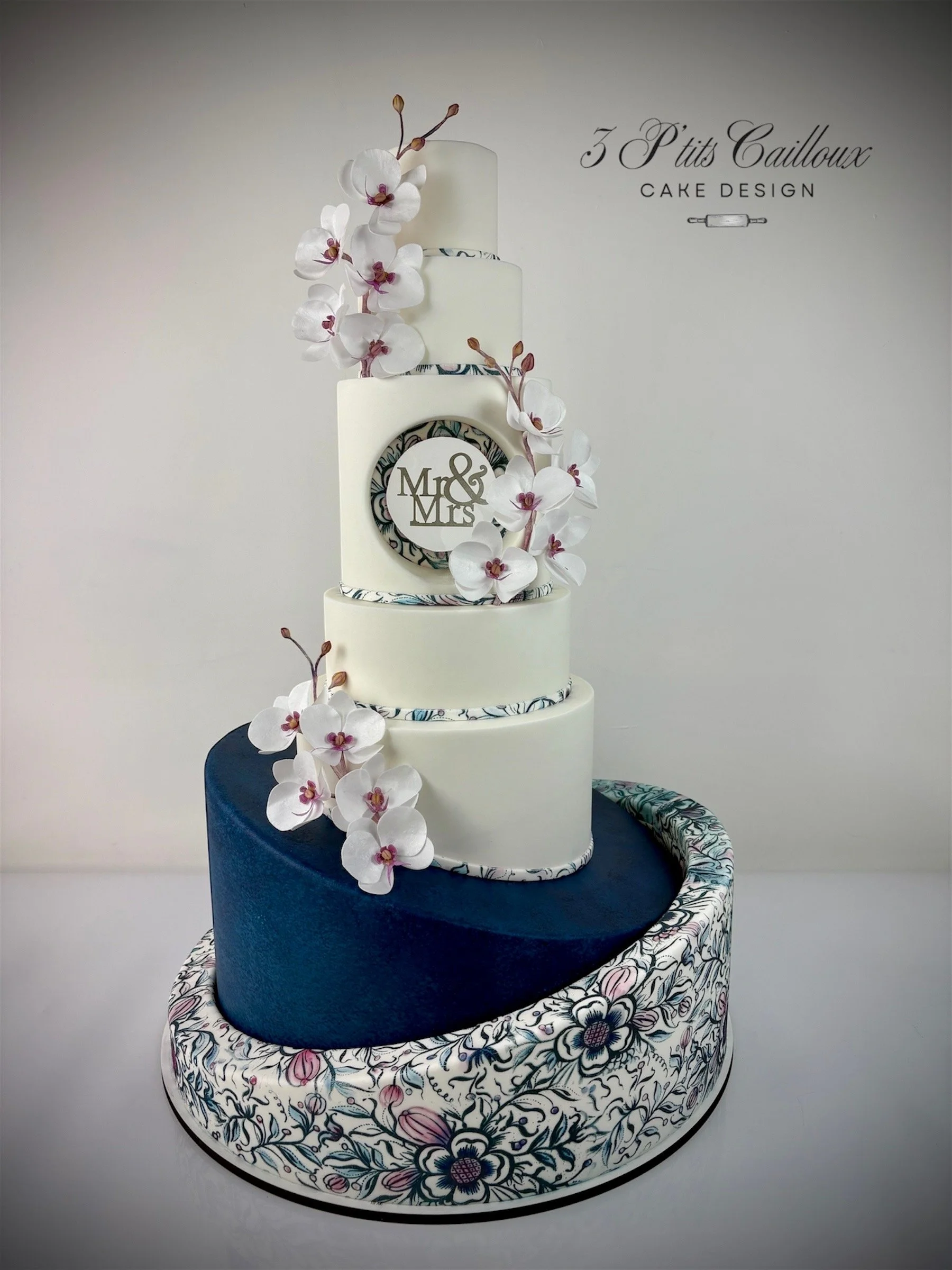 Gâteau de mariage à plusieurs niveaux avec des fleurs orchidées blanches et un disque en sucre avec l'inscription 'Mr & Mrs'.