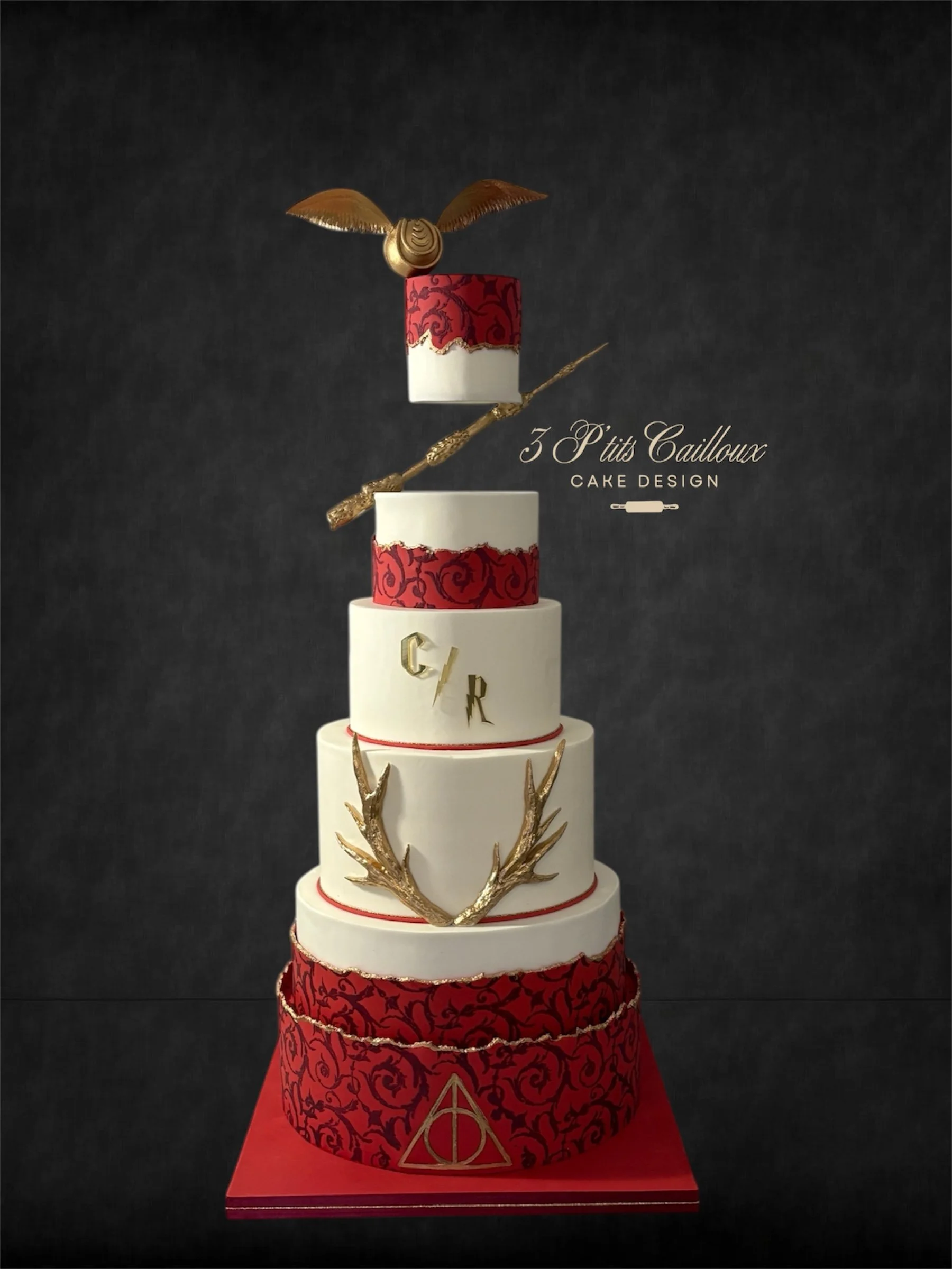 Gâteau de mariage à quatre niveaux, rouge et blanc avec des motifs décoratifs, ornements en or en forme de bois de cerf et un éclair de fée, avec une tête d'aile d'ange en or sur le sommet, sur un fond noir