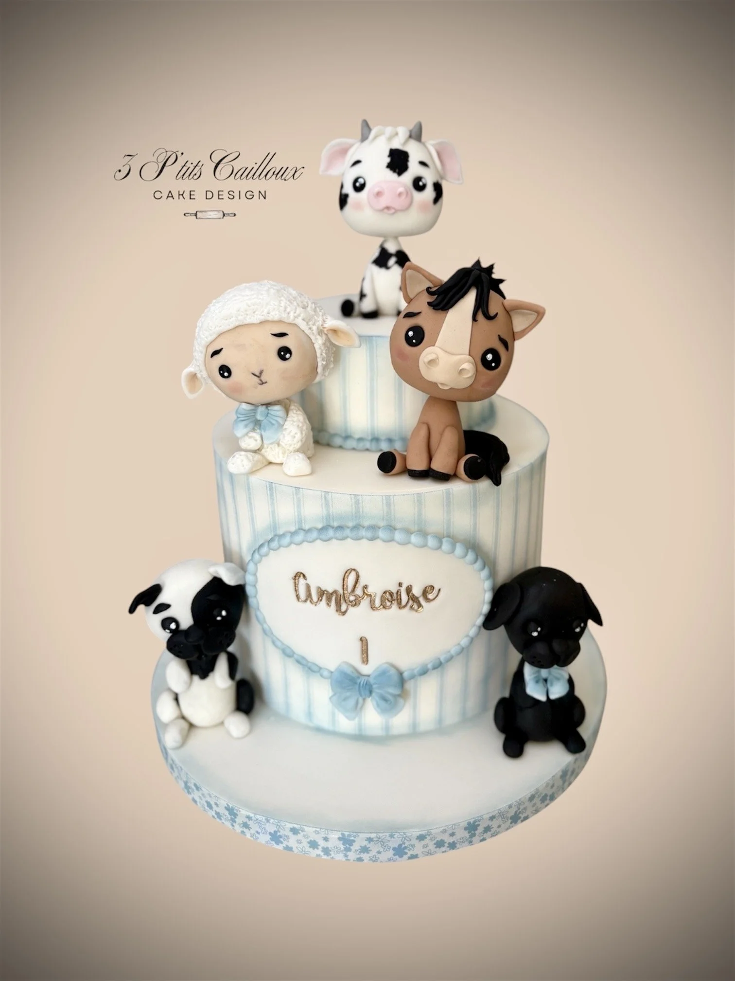 Un gâteau décoré avec des figurines en forme d'animaux, y compris un mouton, un cheval, un cochon, un chien et un chat, avec une inscription 'Ambroise 1' en or.