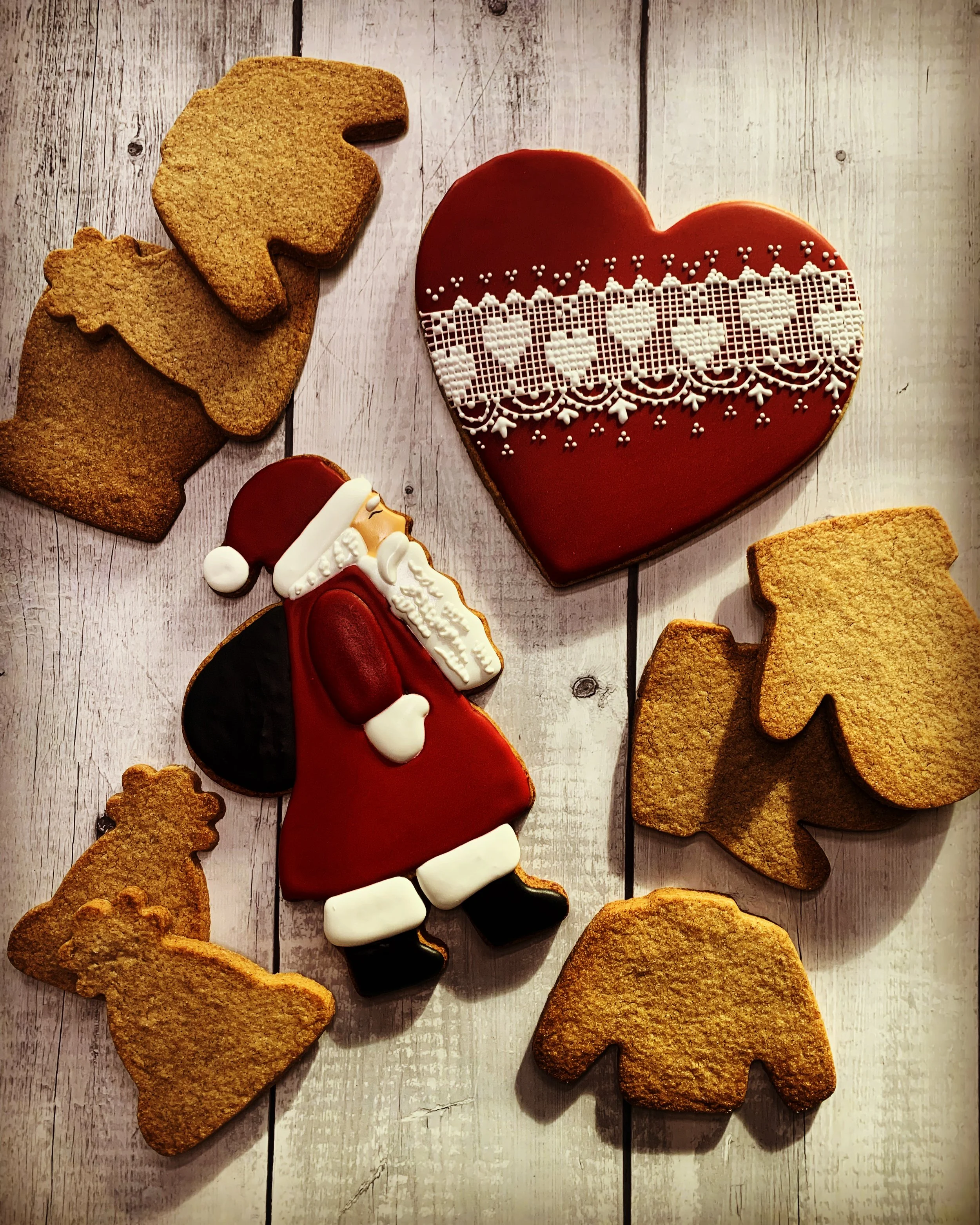 Gâteau en forme de cœur rouge avec décoration en dentelle blanche, biscuits en forme de lutins de Noël, Père Noël en biscuit décoré, et feuilles d'automne en biscuits sur un fond en bois clair.