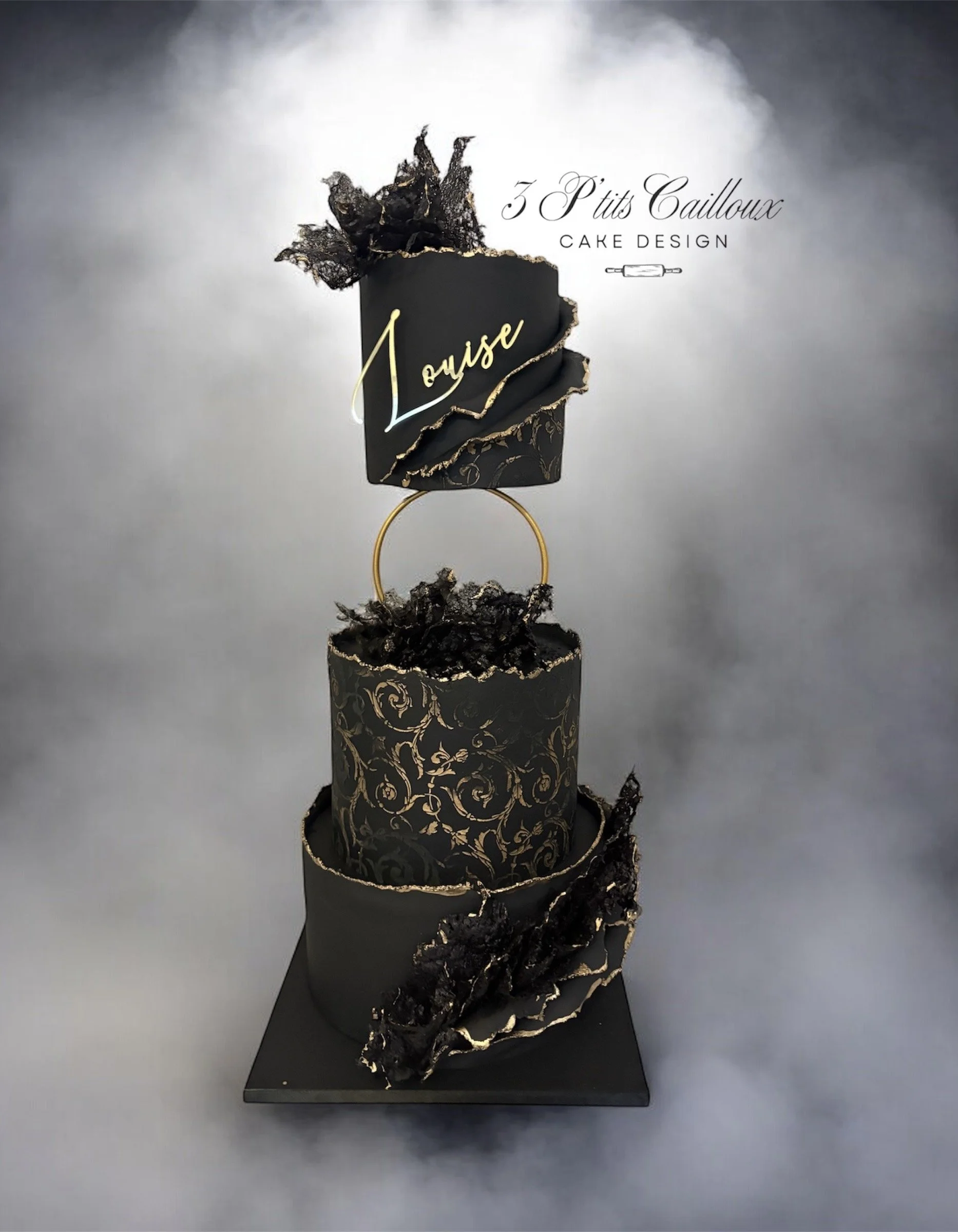 Gâteau noir à trois niveaux avec décoration en papier mâché noir et or, inscriptions et éléments décoratifs élégants, présenté pour une occasion spéciale
