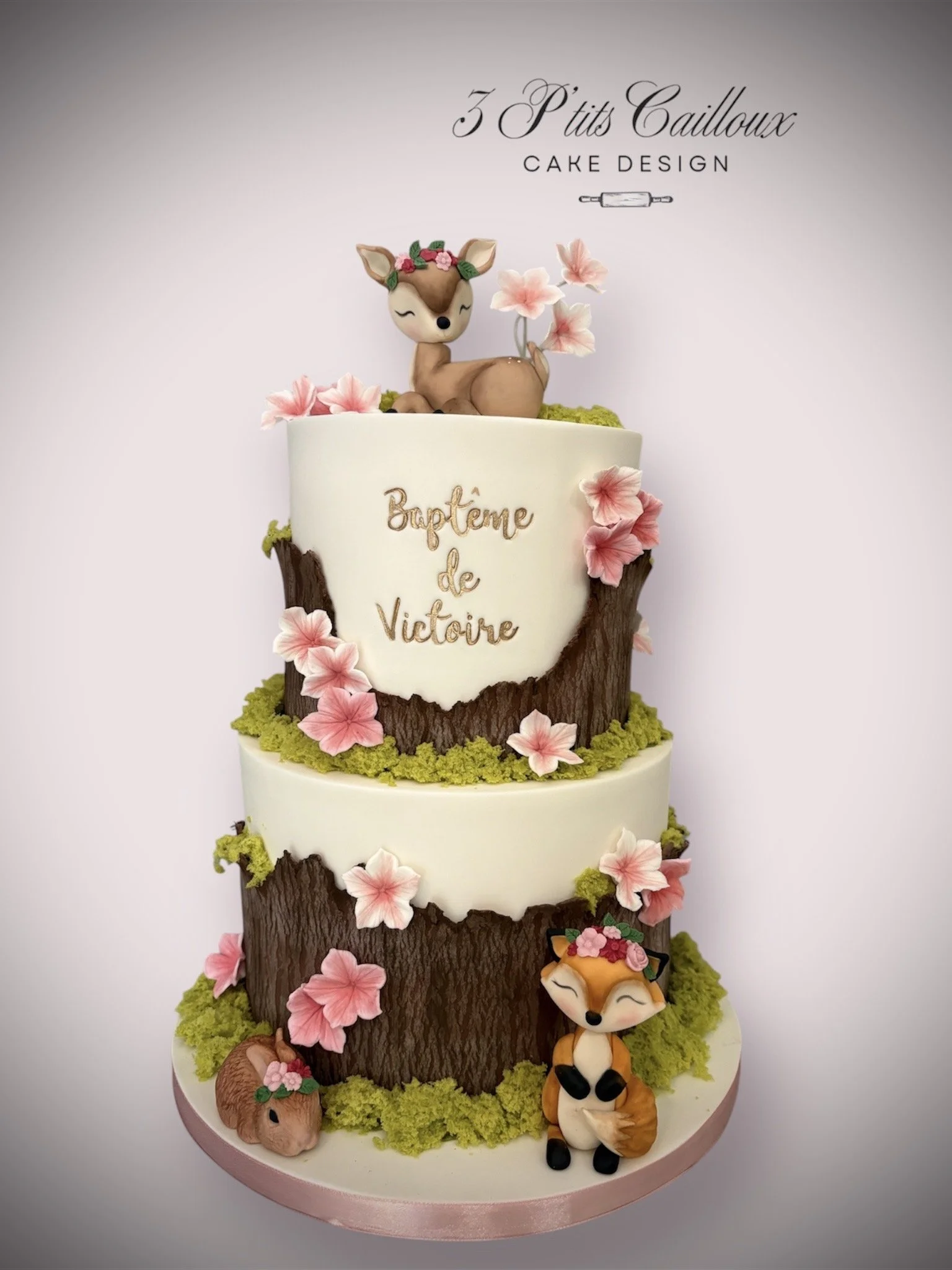 Gâteau en forme d'arbre avec des décors de fleurs roses et de personnages animaux en pâte à sucre, avec un message en français. 