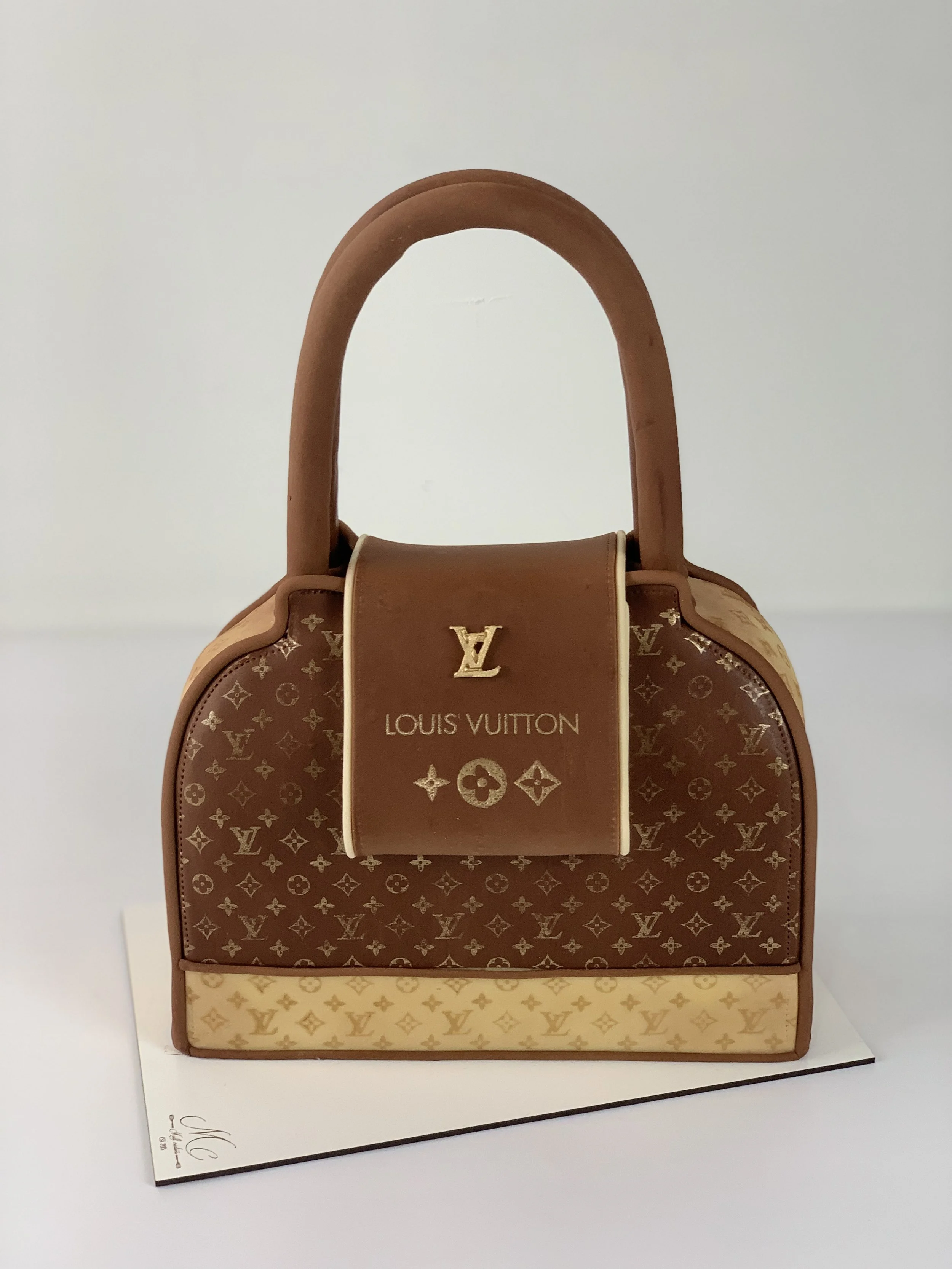 Sac à main Louis Vuitton en simili cuir avec monogramme classique et poignée beige, posé sur une surface blanche.