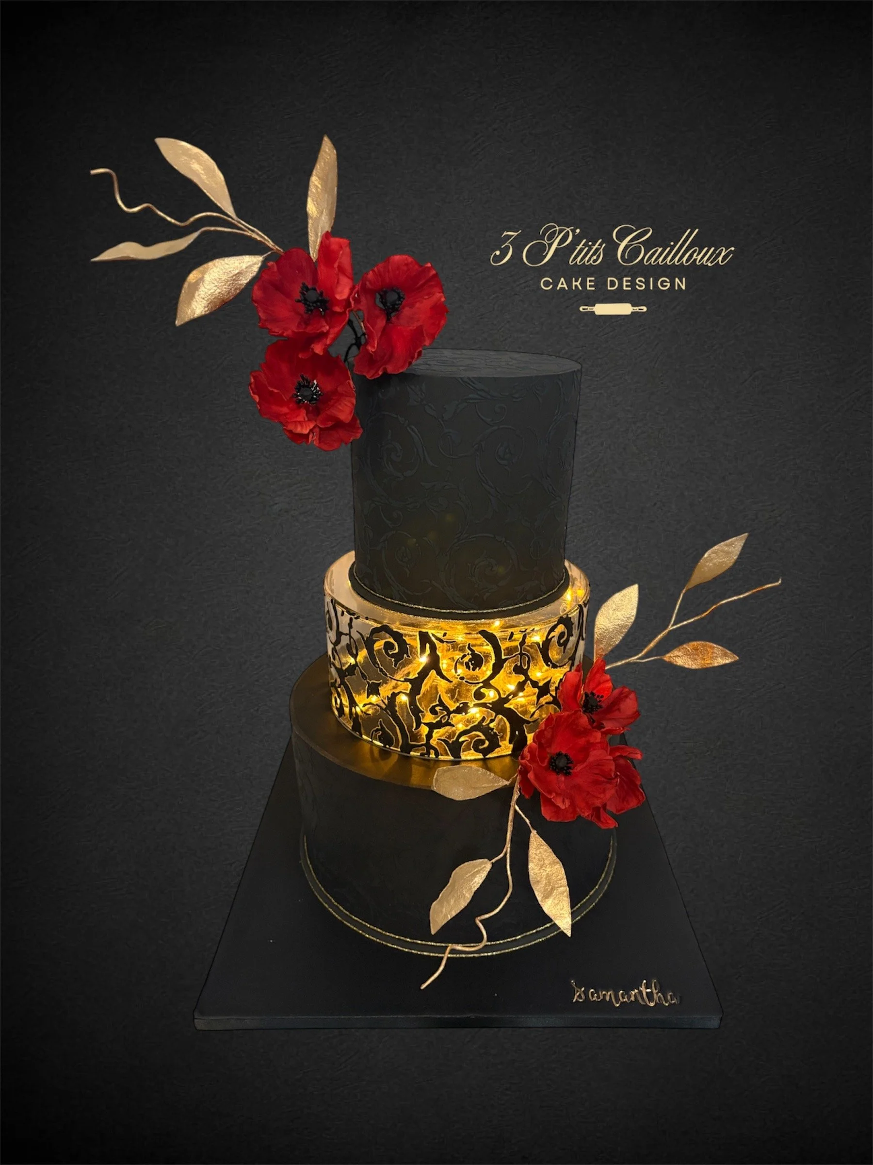 Gâteau noir avec décorations dorées, fleurs rouges et feuilles dorées, portant le texte "3 P'tits Cailloux Cake Design".