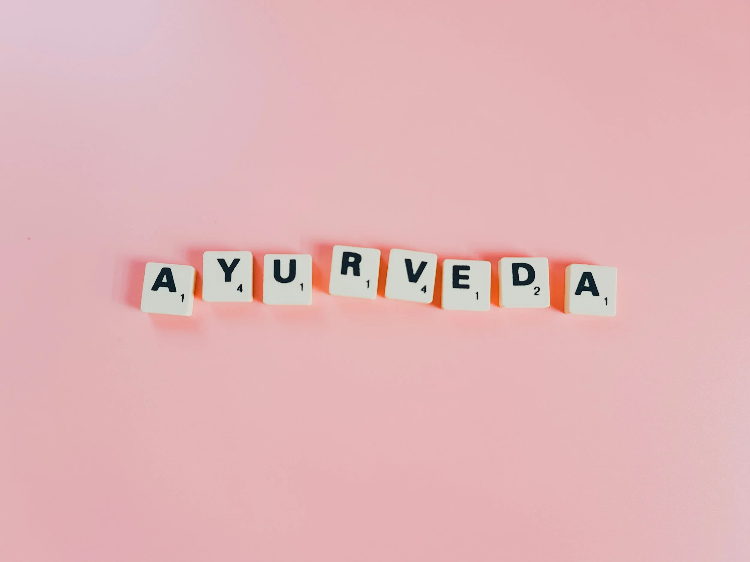The word Ayurveda spelled out with letter tiles on a pink background