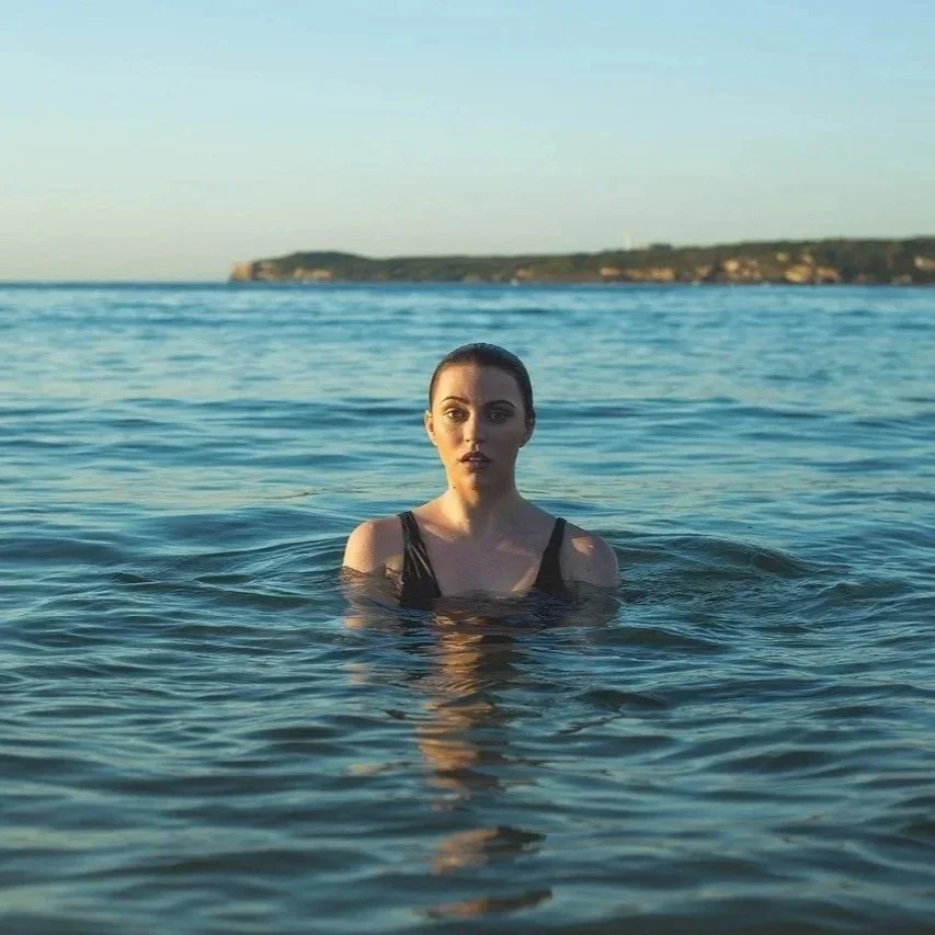 Woman swimming in cold open water with a coastline in the background