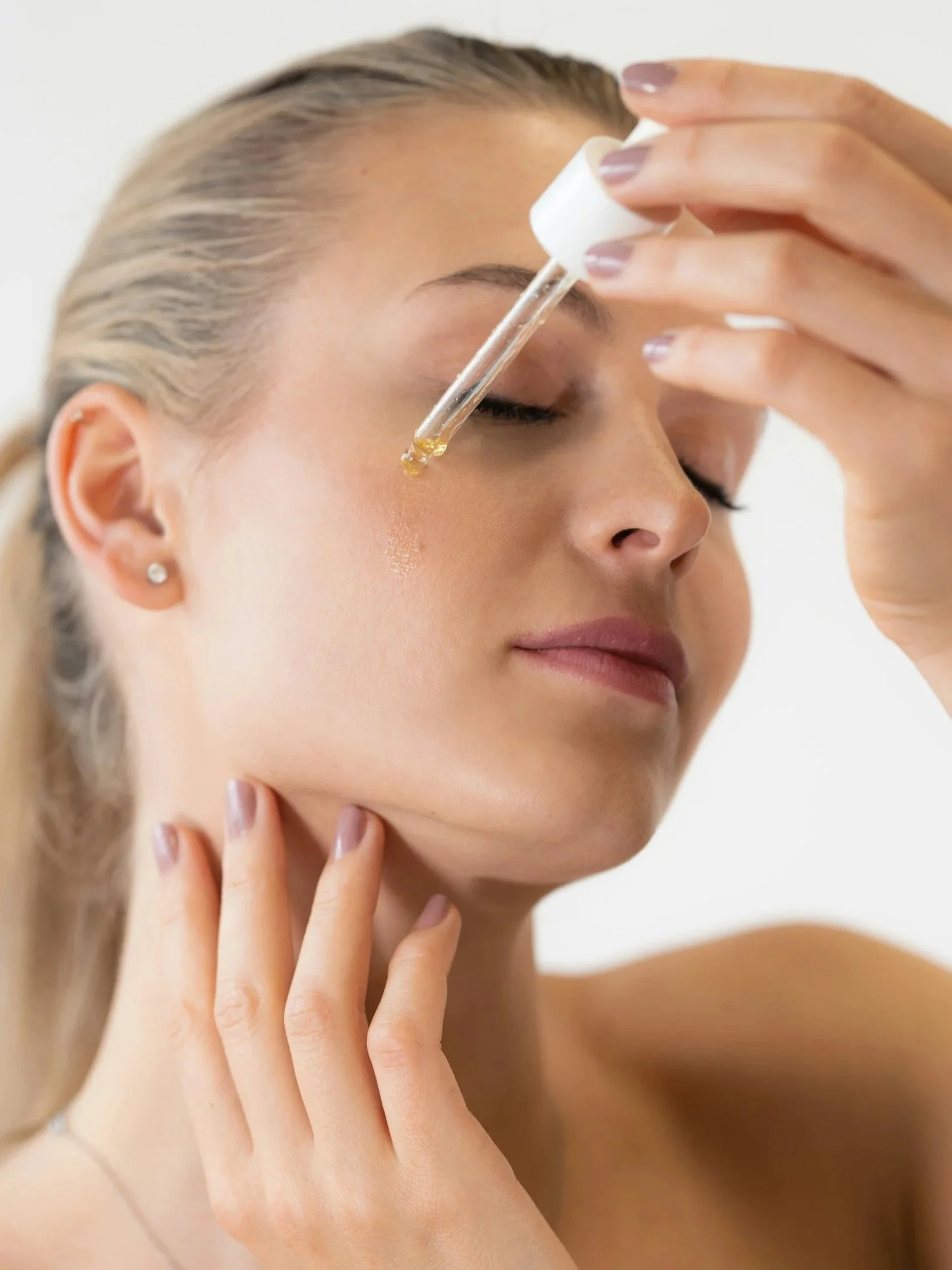 Woman applying facial serum with a dropper as part of her skincare routine.