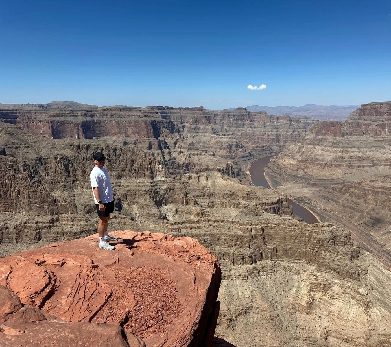 A person standing on a red rock ledge overlooking the Grand Canyon on a clear, sunny day.