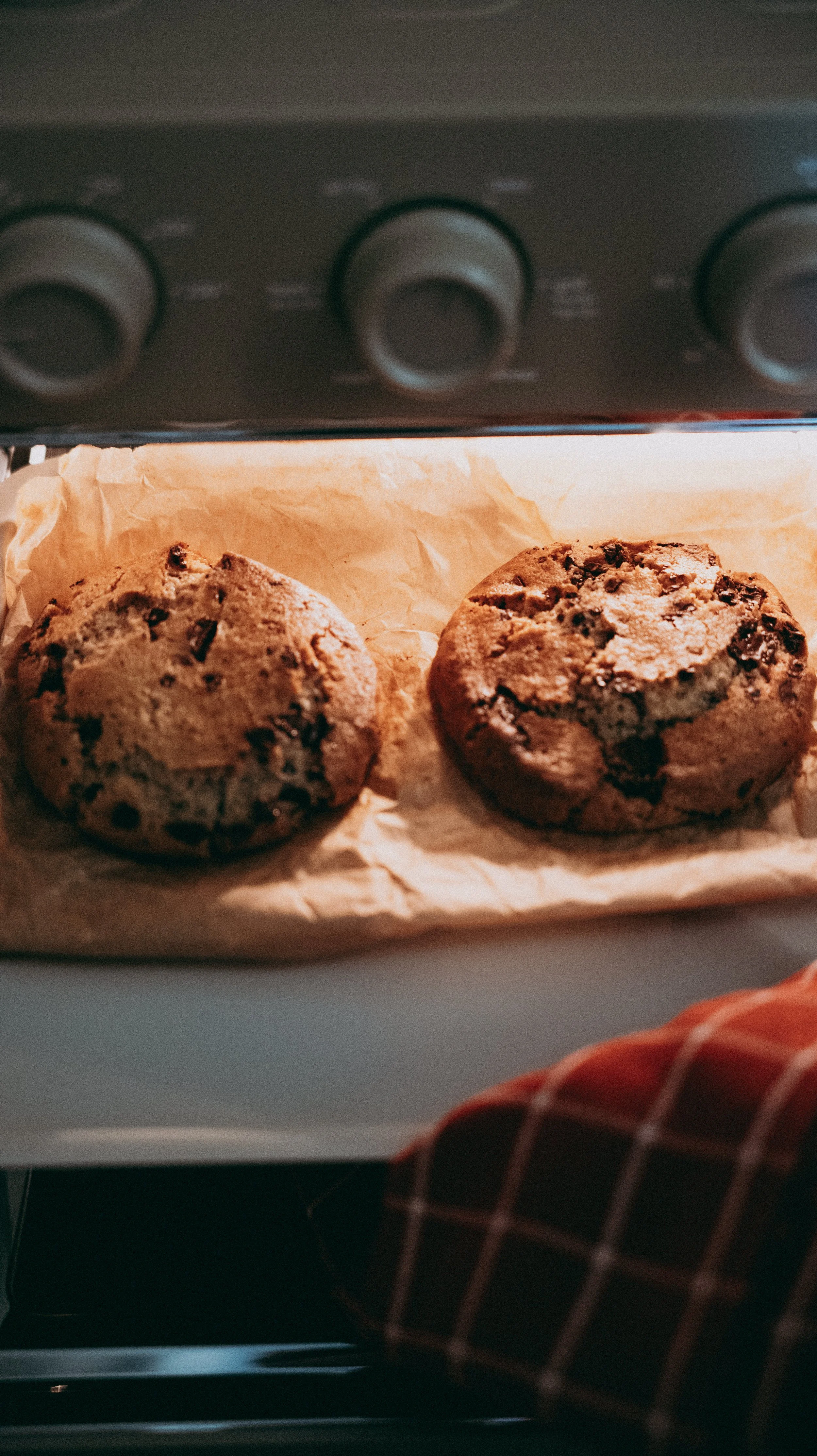 Two chocolate chip cookies on parchment paper inside an Our Place wonder oven.