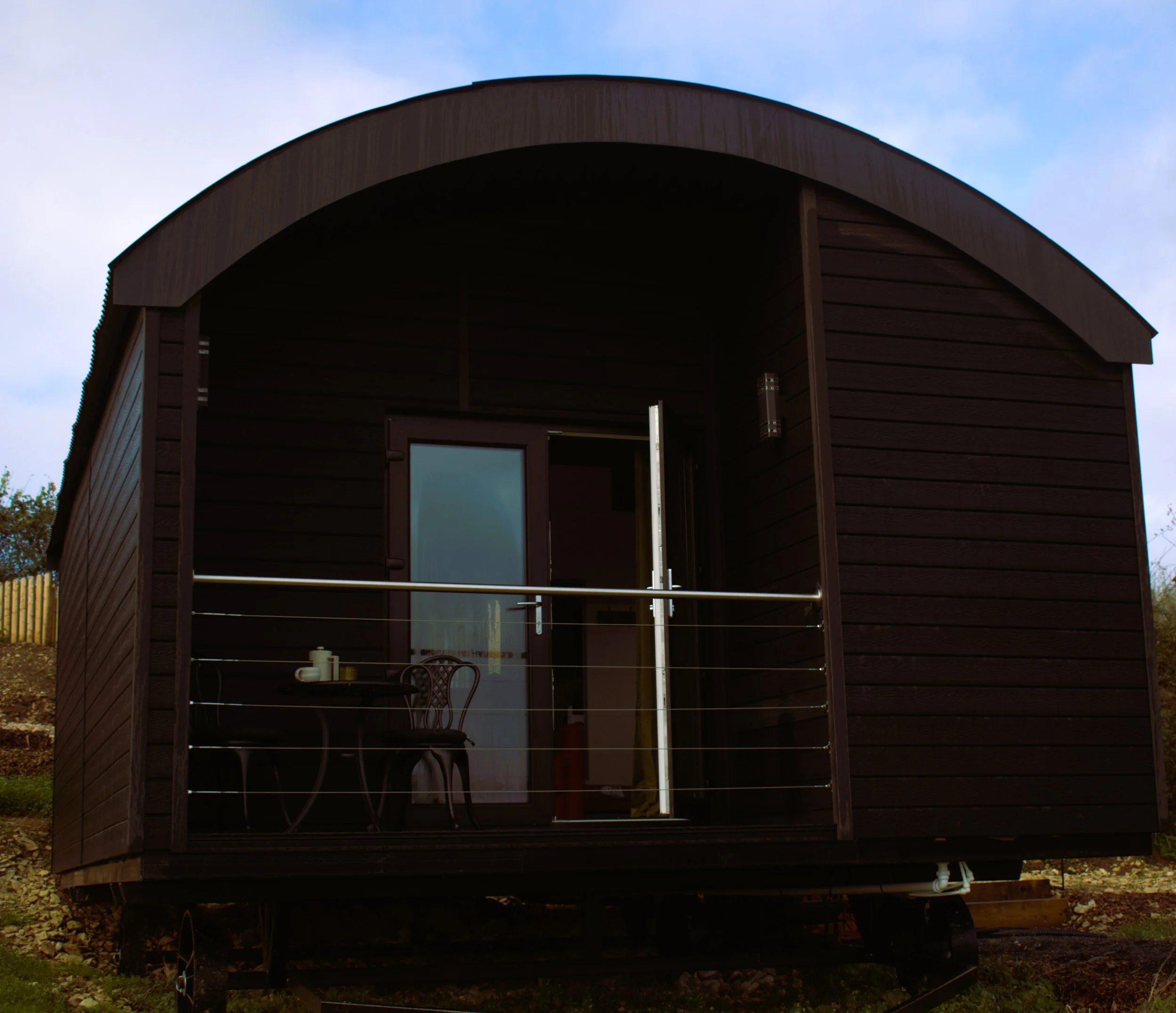 A cabin with an arched roof and open balcony door. The sky is partly cloudy with some blue visible.