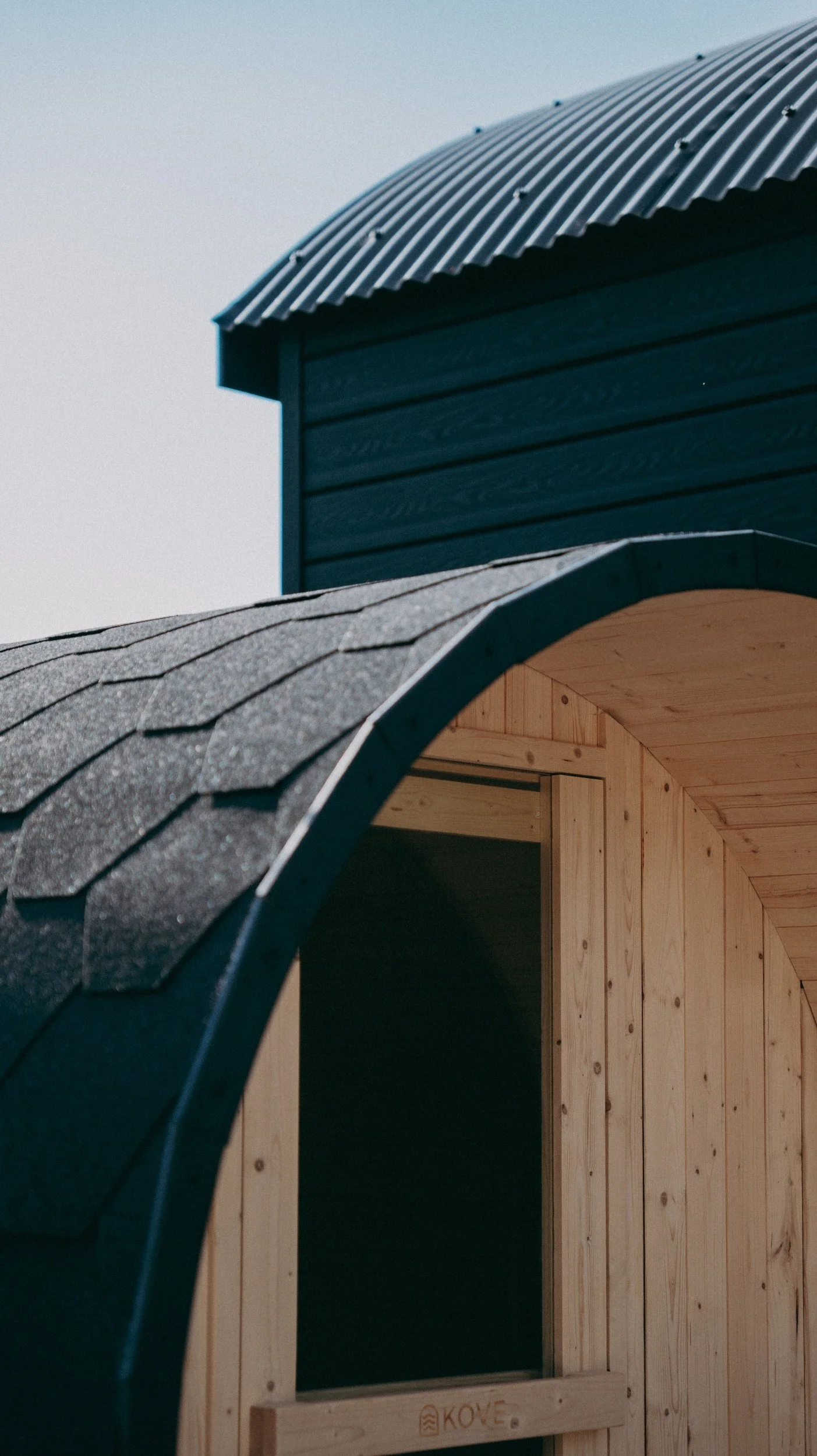 Close-up of a black sauna roof with black shingles, and part of a black cabin in the background.