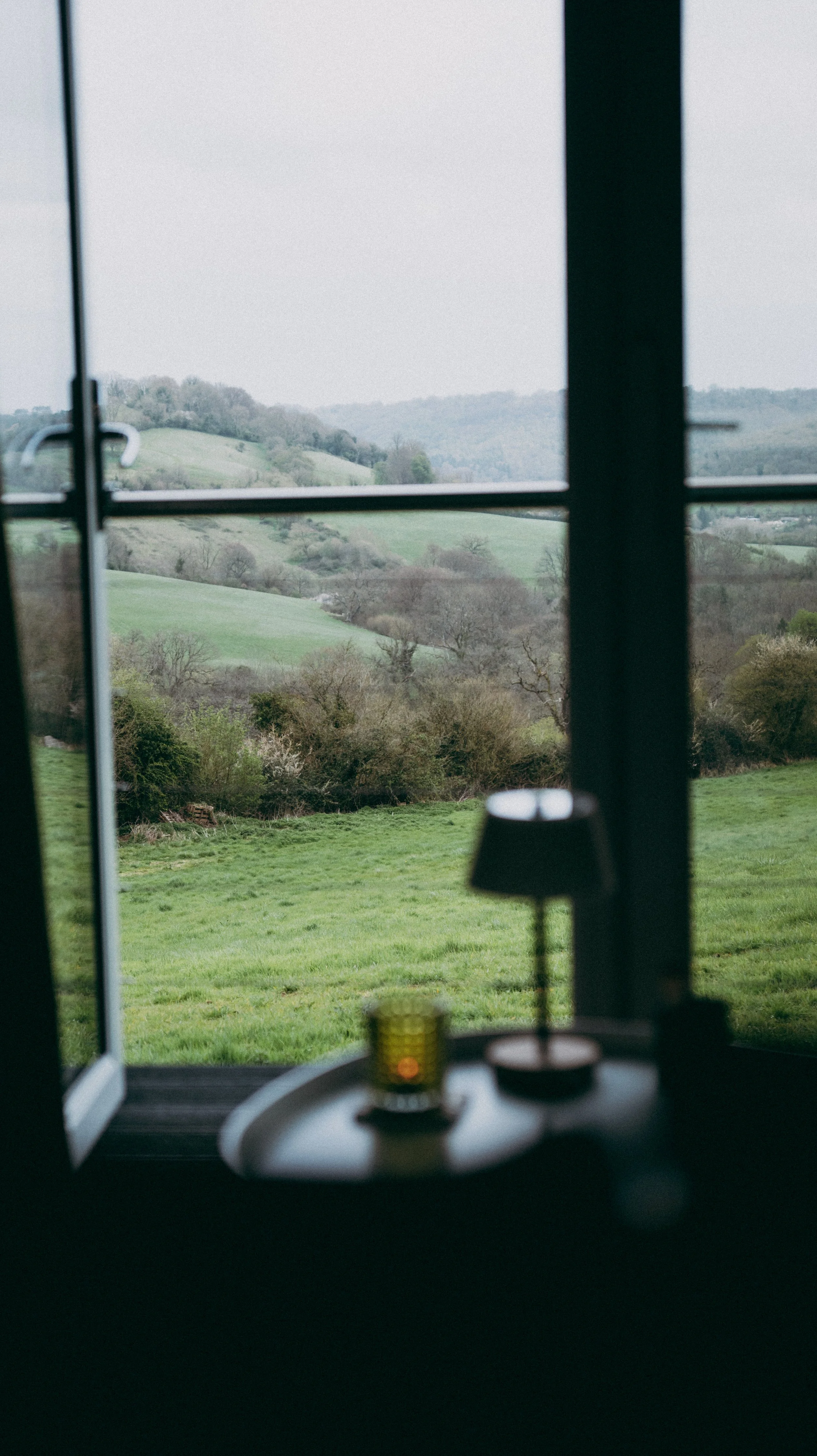 View of rolling green hills and trees outside a door to a balcony, with a coffee table cabin interior scene in the foreground.