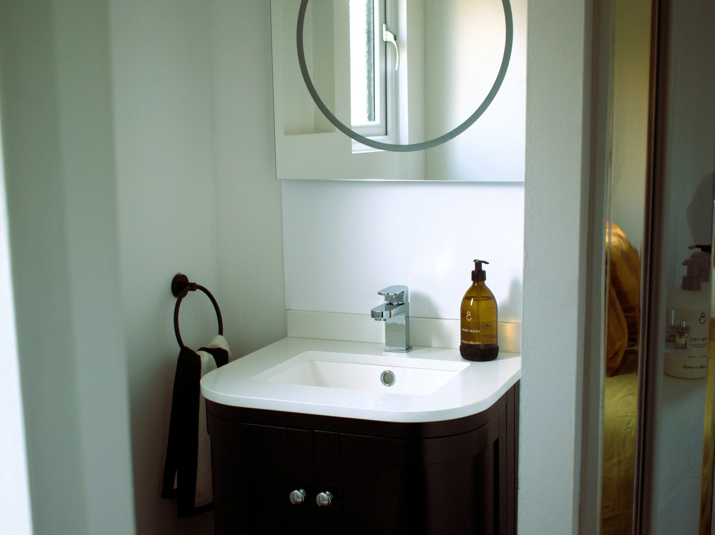 Bathroom sink with a mirror, a small window, and a soap dispenser on the countertop.