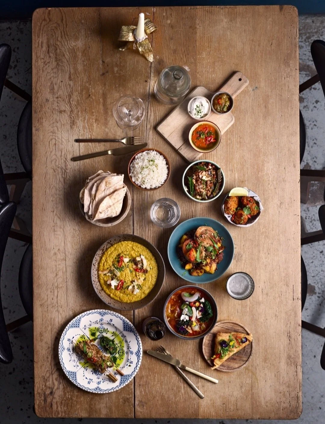 A top-down view of a wooden table set with various Indian dishes, including bowls of rice, curry, roti and side dishes.
