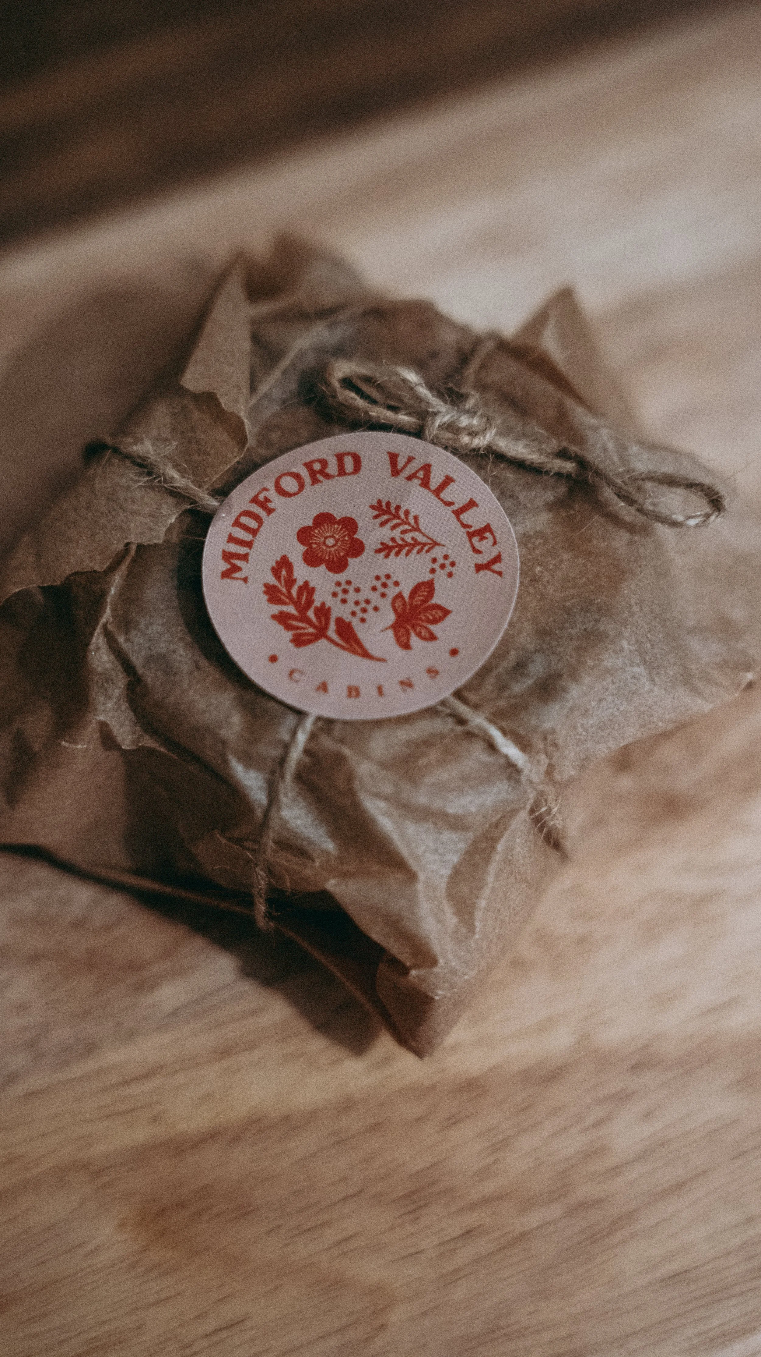Cookie dough wrapped in brown paper with string tied around it, featuring a circular label with red floral and leaf designs reading 'Midford Valley Cabins.'
