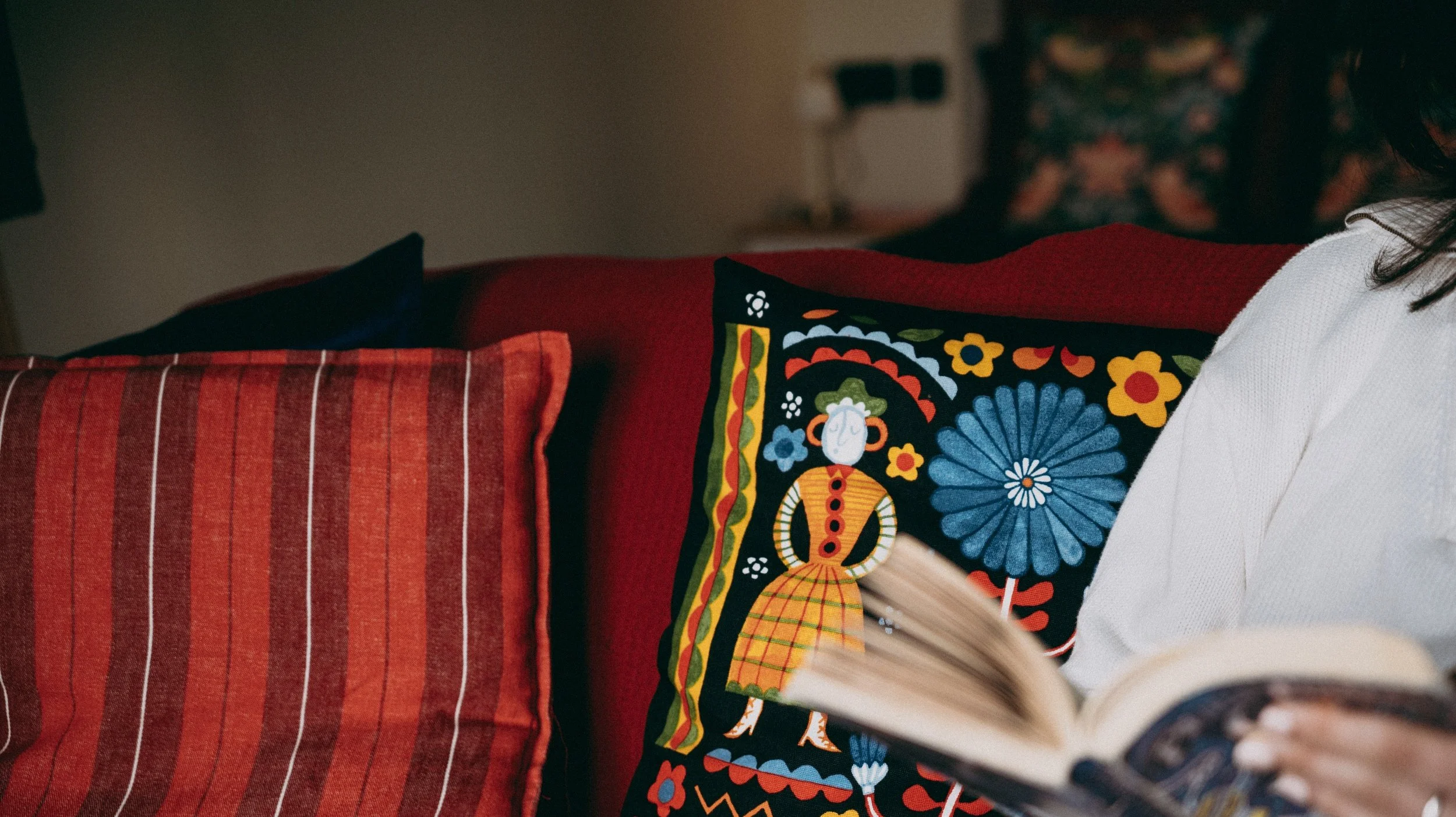 Close-up of a colorful decorative cushion with a traditional folk art pattern, placed on a red striped couch.