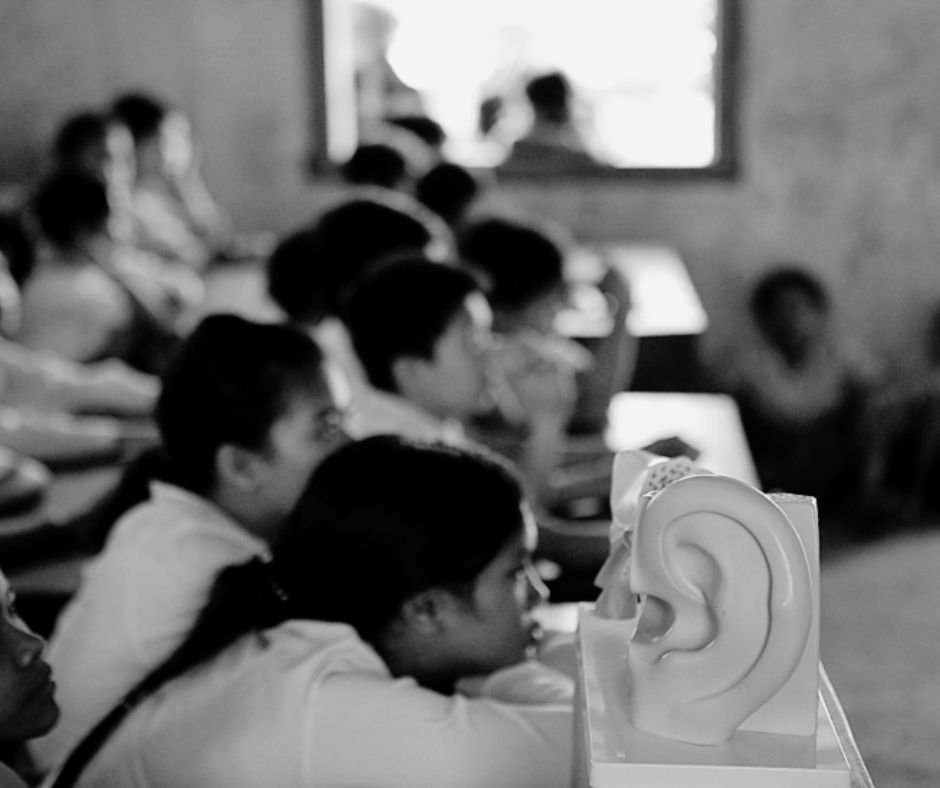 Students in a classroom watching a presentation, with a model of a human ear in the foreground.