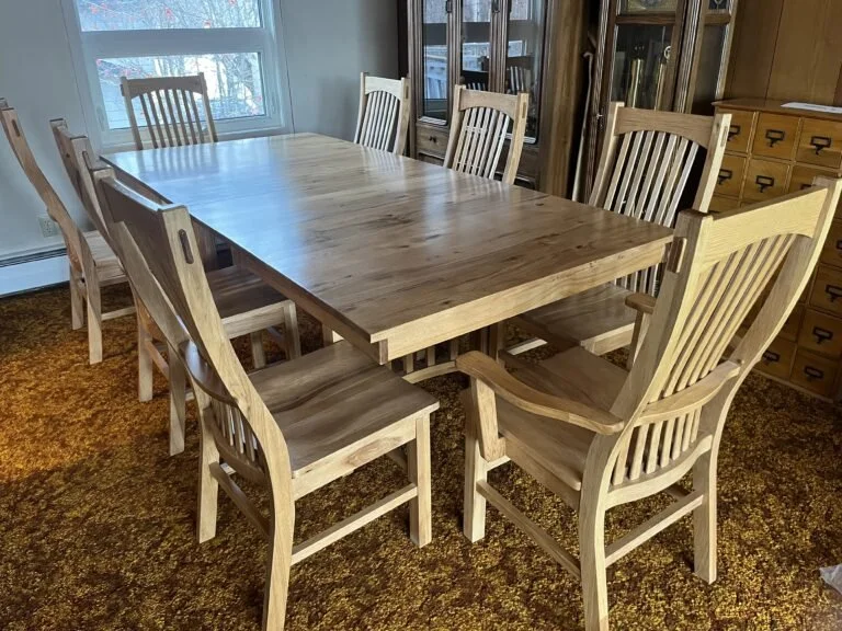 Wooden dining table surrounded by eight matching wooden chairs in a dining room with windows, a display cabinet, and a wooden drawer cabinet from estate sale in Anchorage, Alaska and the Mat-Su area
