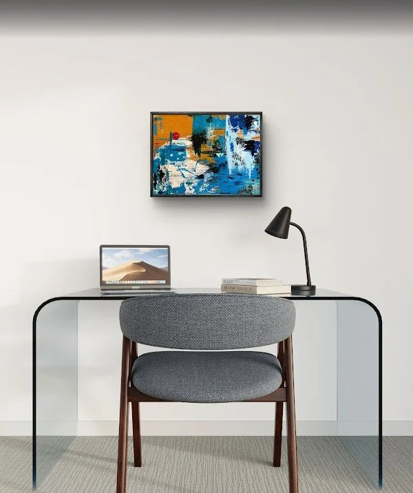 Modern home office setup with a sleek black desk, gray upholstered chair, laptop, black desk lamp, and colorful abstract painting on a white wall.