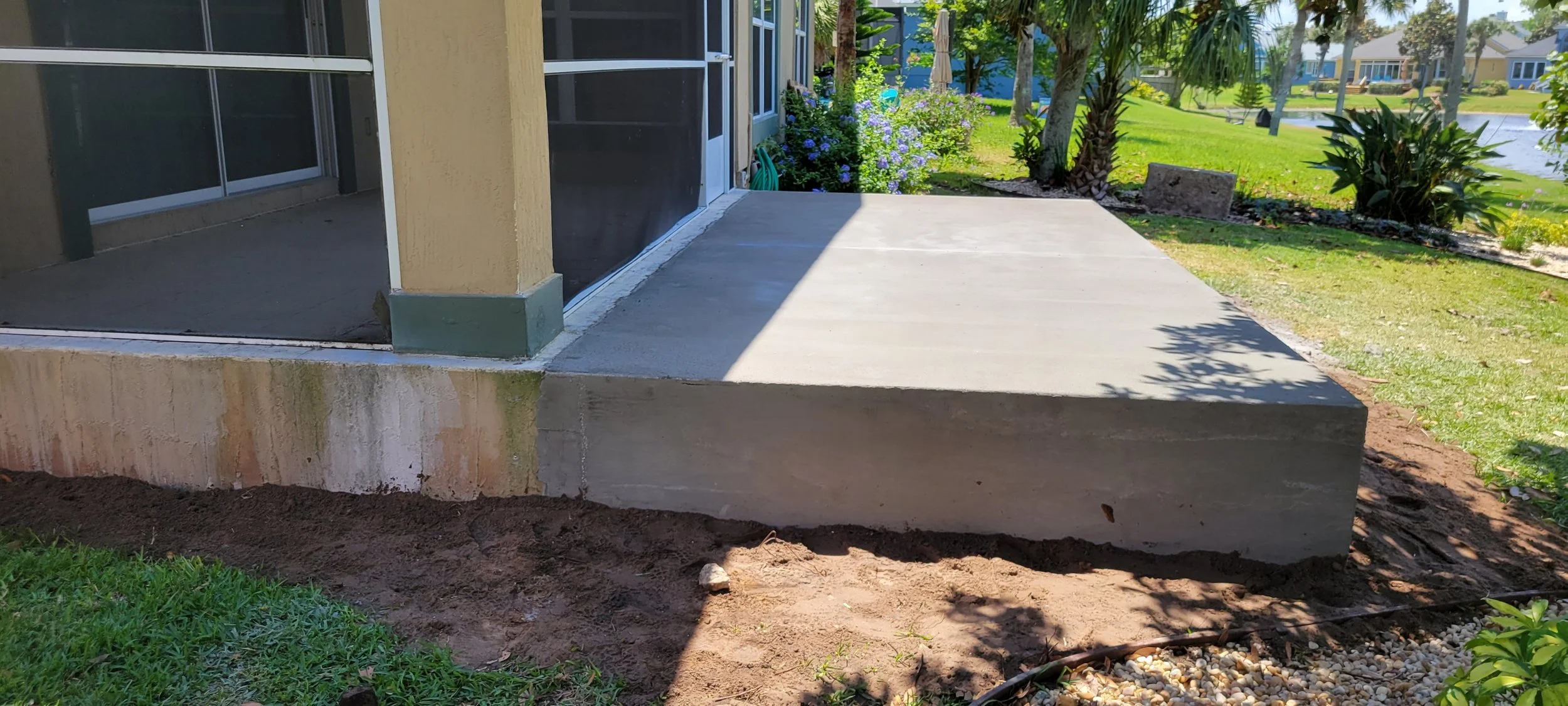 Concrete porch pad in a backyard next to a screened door and sliding glass door, surrounded by grass, plants, and trees.
