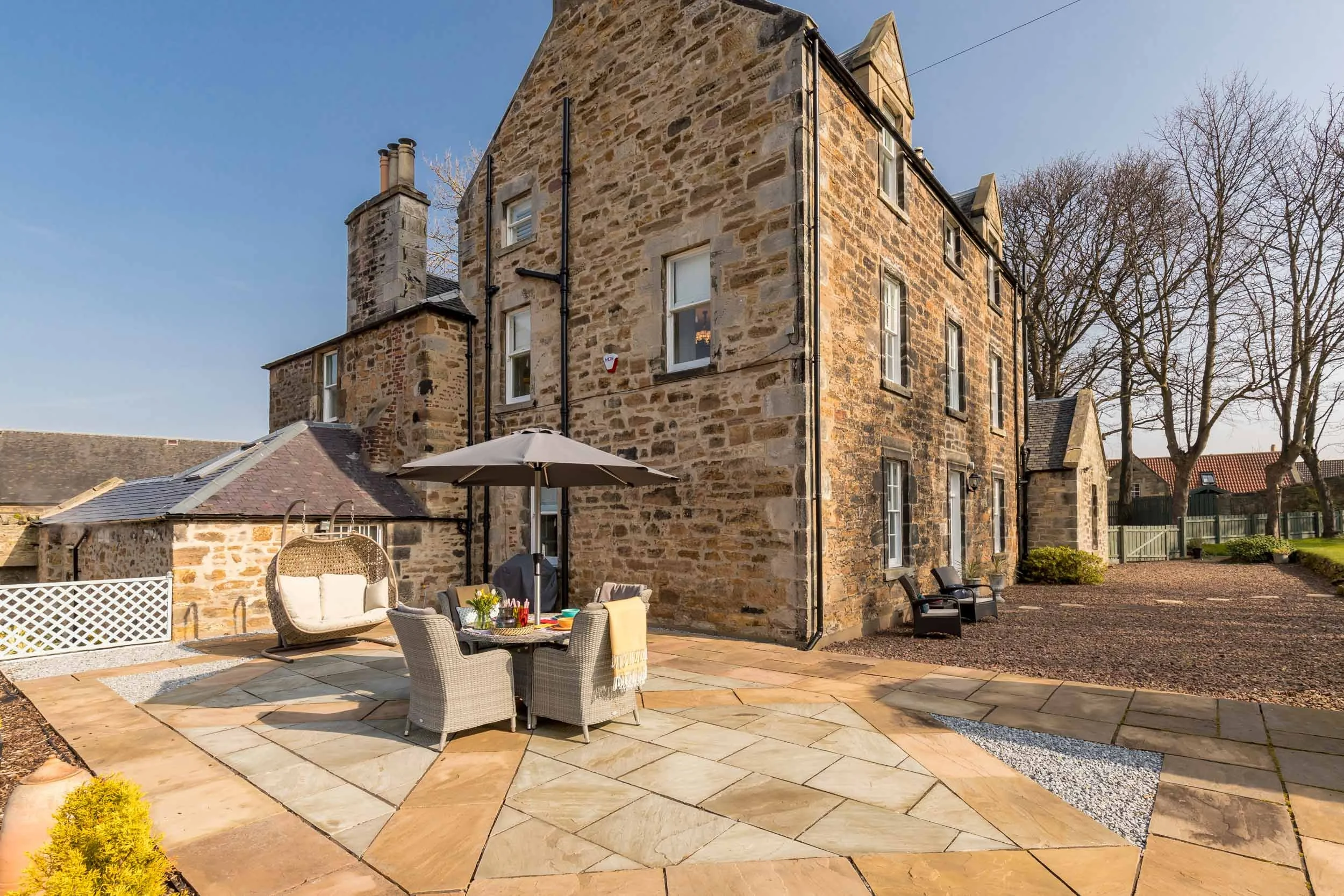 Stone house with outdoor patio, table, chairs, large umbrella, and garden seating area.