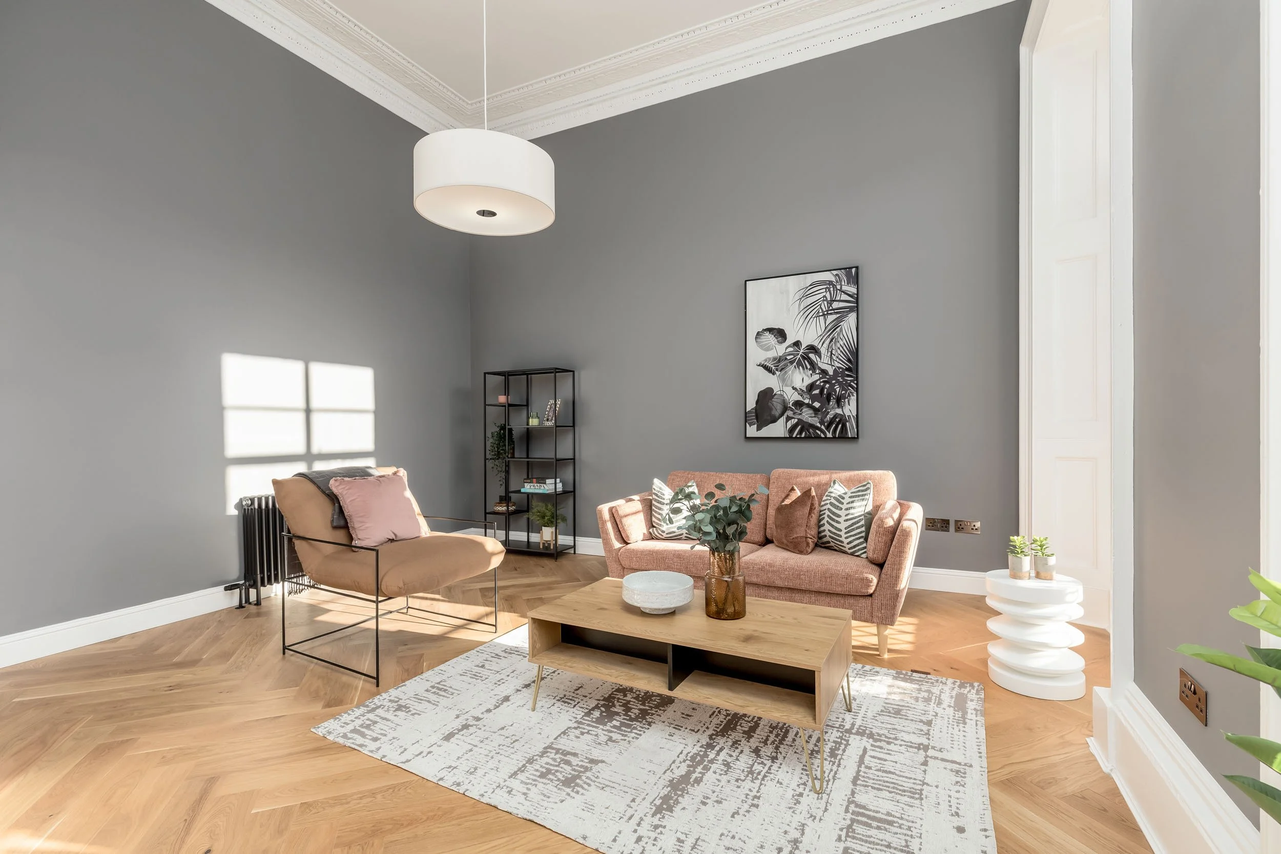 Living room with gray walls, pink sofa, beige chair, wooden coffee table, white rug, art on the wall, and sunlight through window