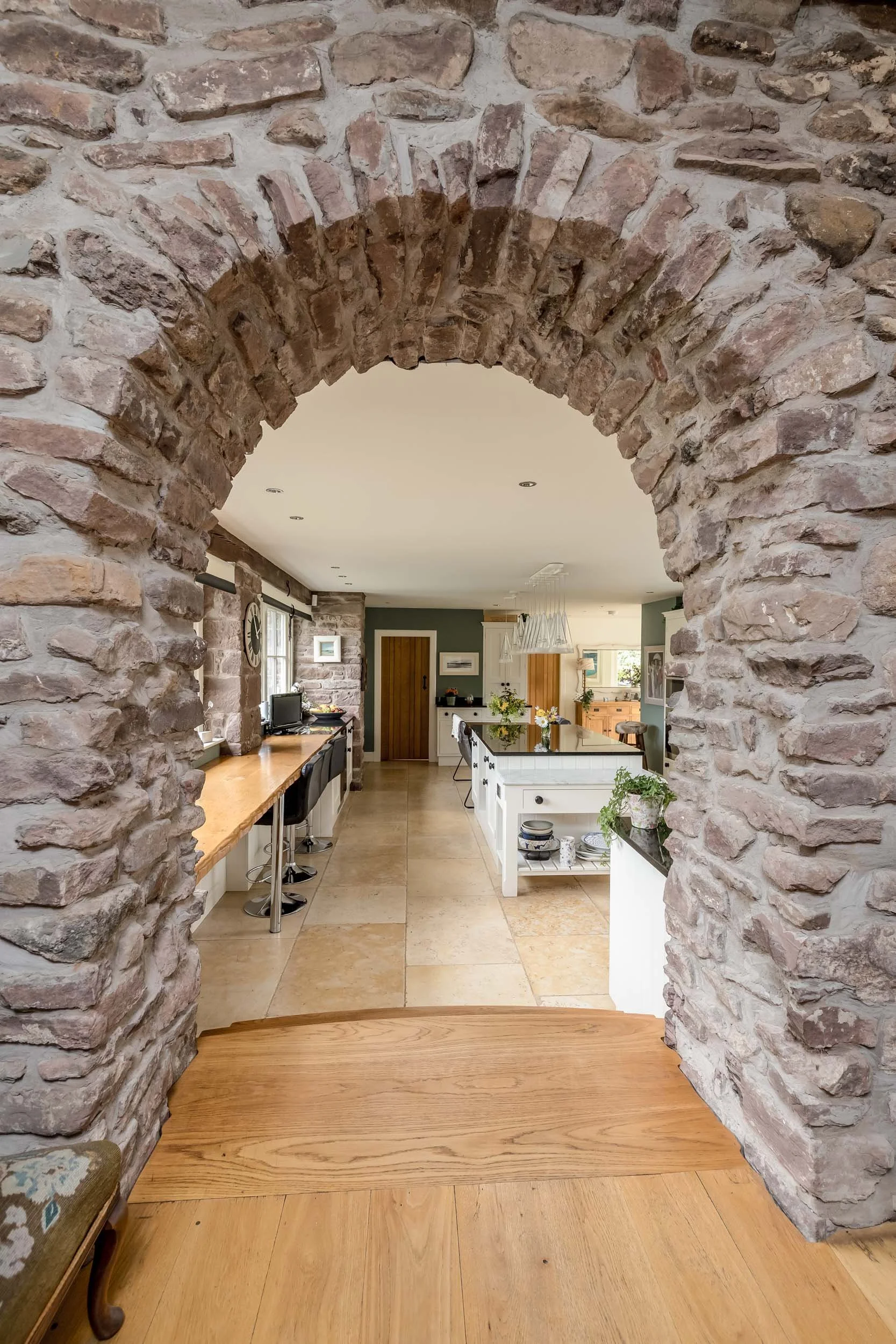 Rustic stone archway opening into a modern kitchen with a large island, wooden accents, and green walls.