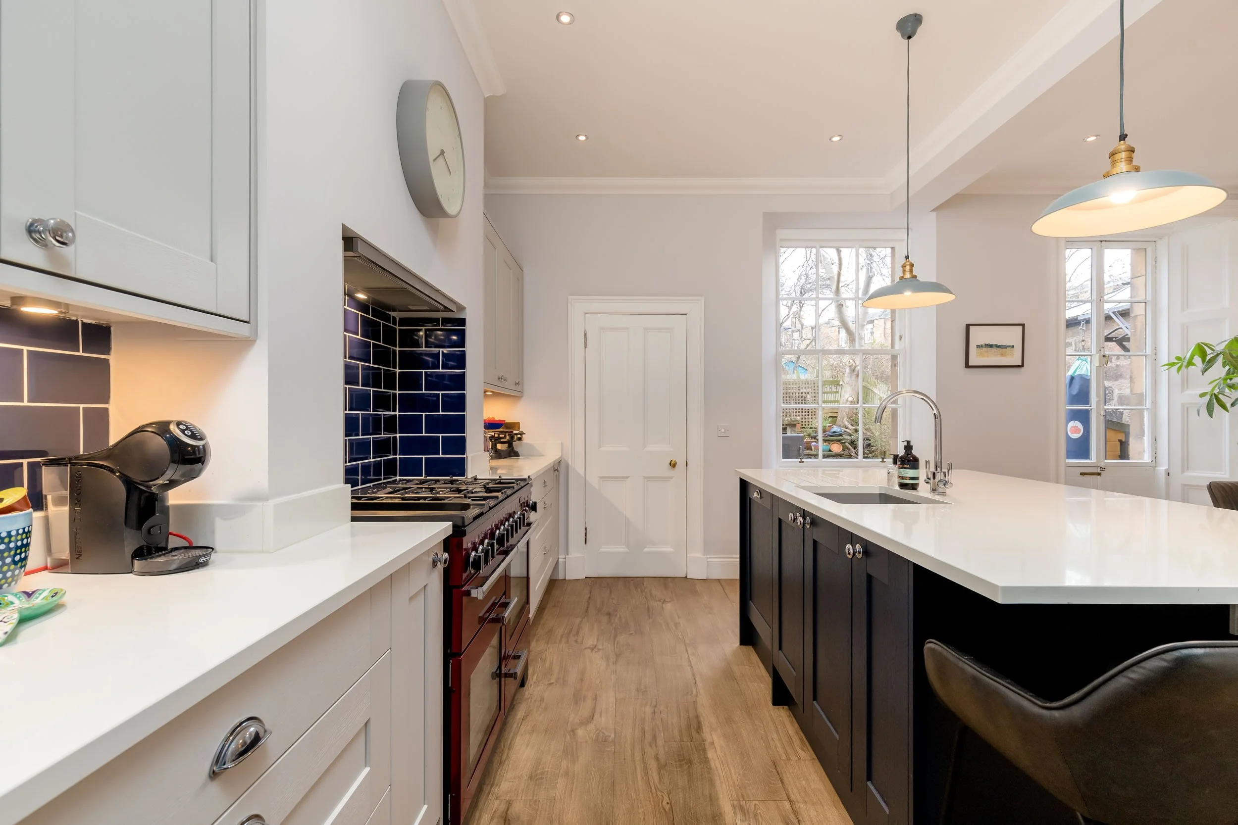 Modern kitchen with white and black cabinets, wood flooring, a large island with a sink, and windows showing a backyard.