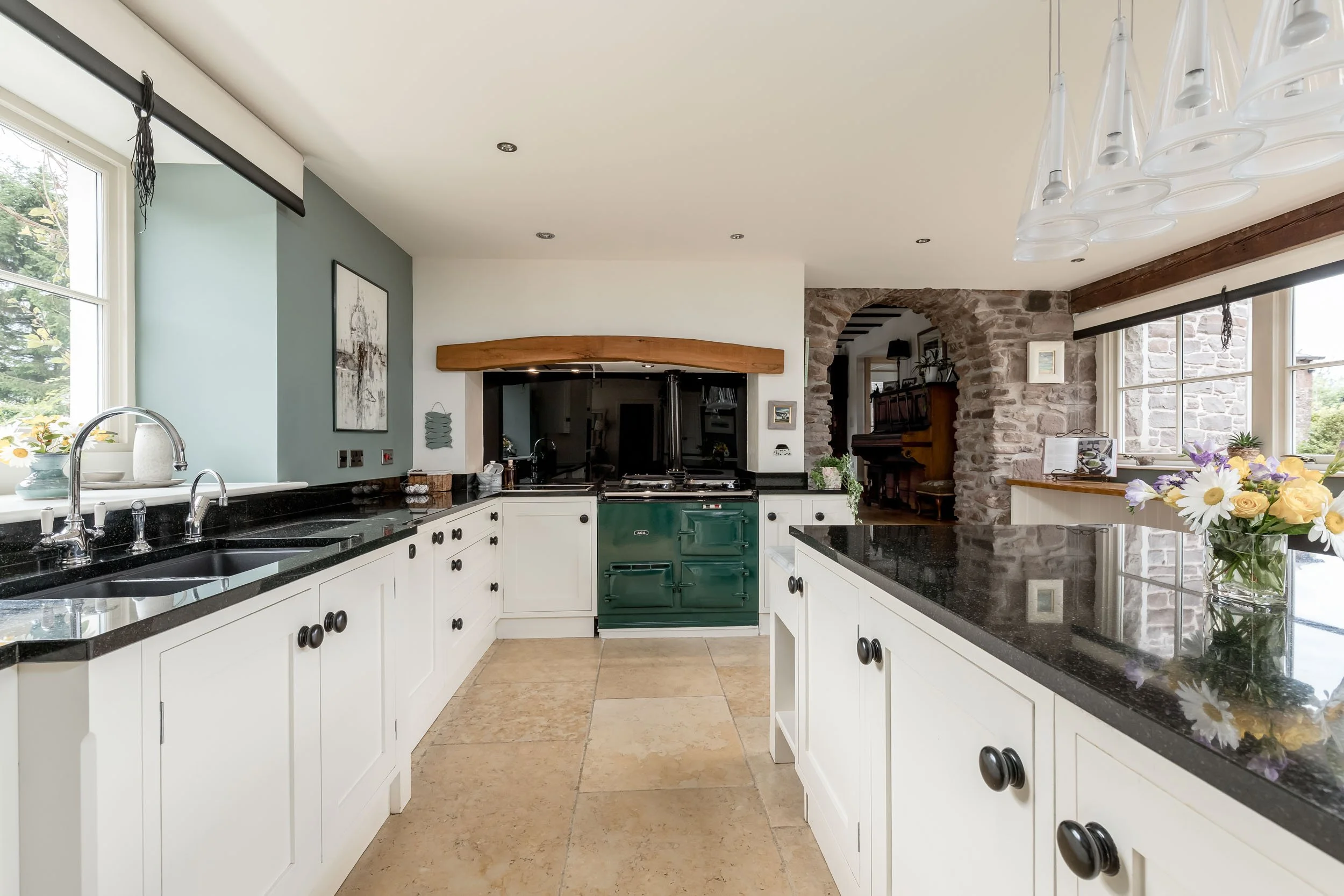 Modern kitchen with white cabinets, black countertops, a green vintage stove, large windows, and a stone archway leading to a cozy room.