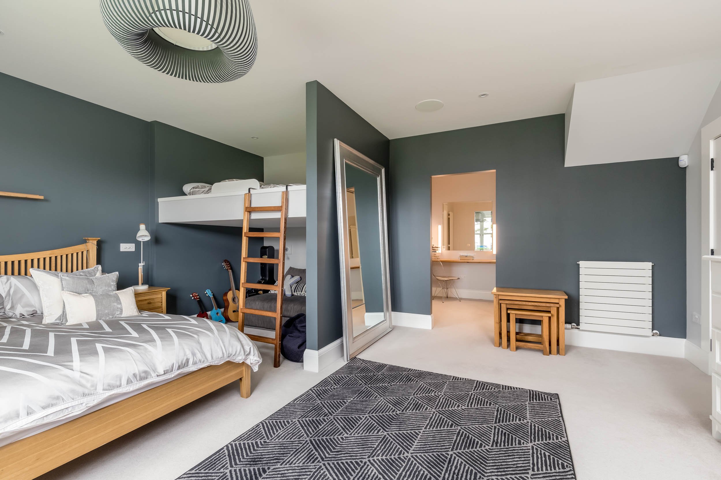 A bedroom with a bed, a large mirror leaning against the wall, a bunk bed, and a small stack of nesting tables. There are guitars beside the bed and a patterned rug on the floor.