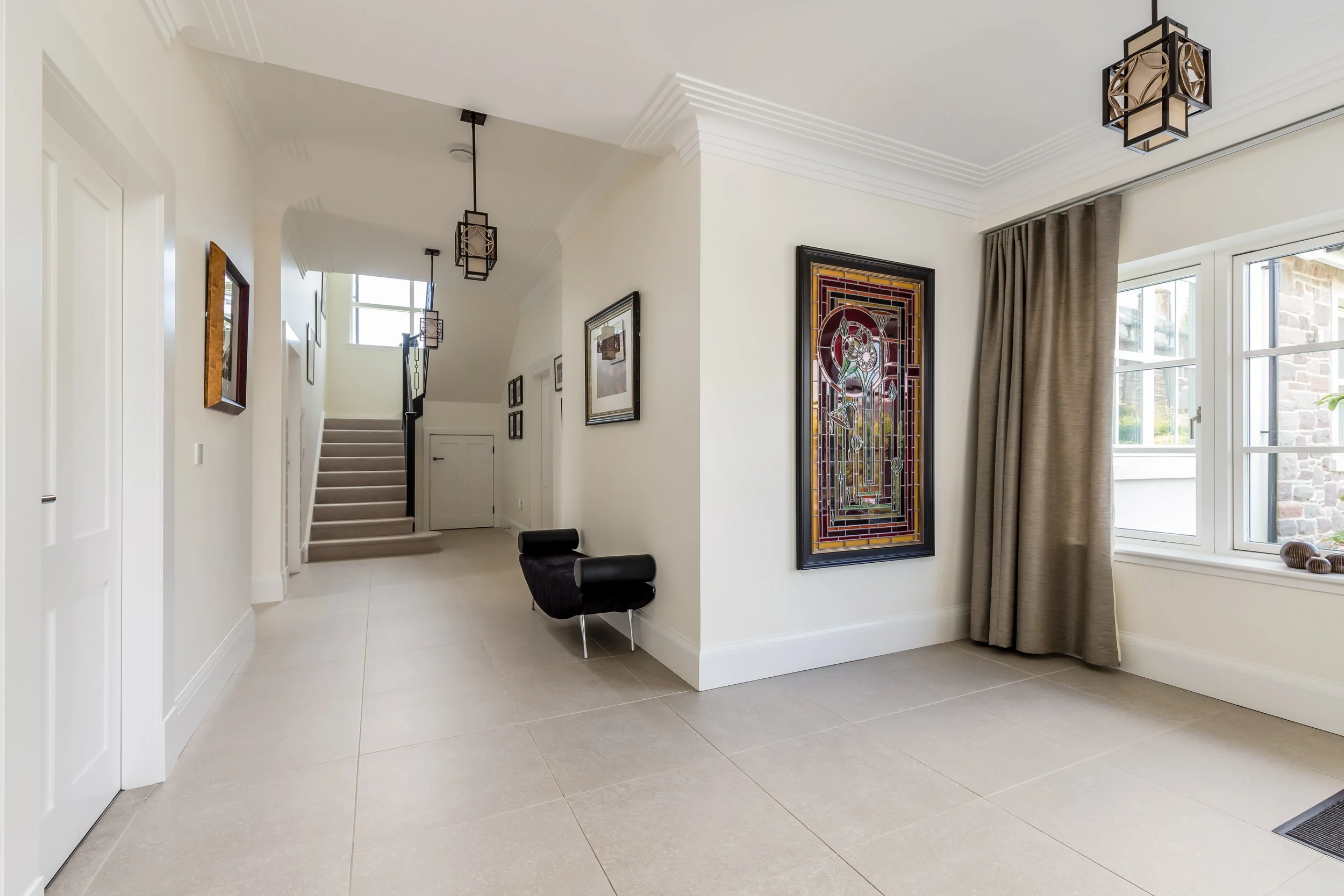 Entryway with white walls, beige tile floors, wall art, a black bench, a large window with curtains, and pendant light fixtures.