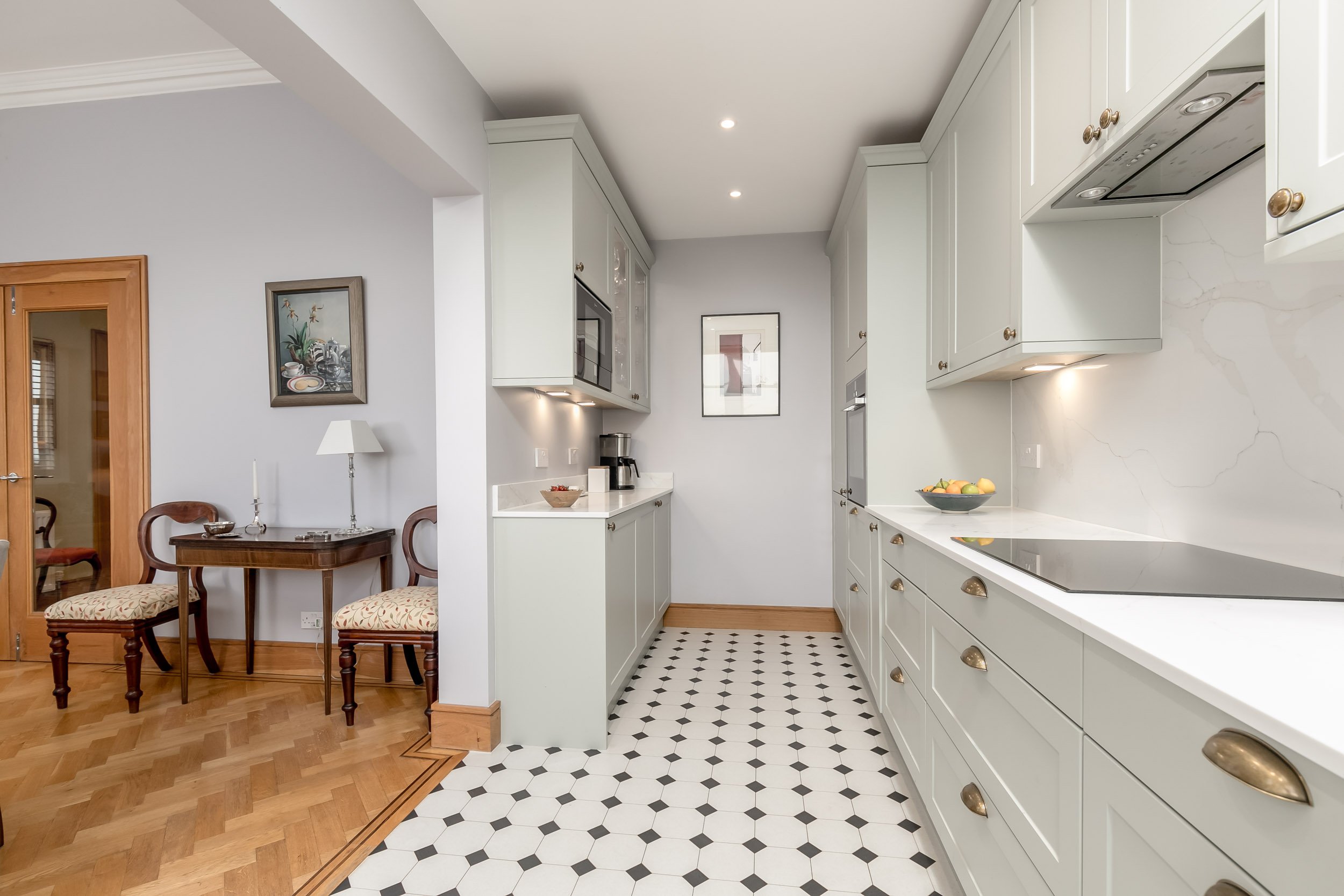 Kitchen with white cabinets, black and white hex tile floor, and wooden dining table with two chairs.
