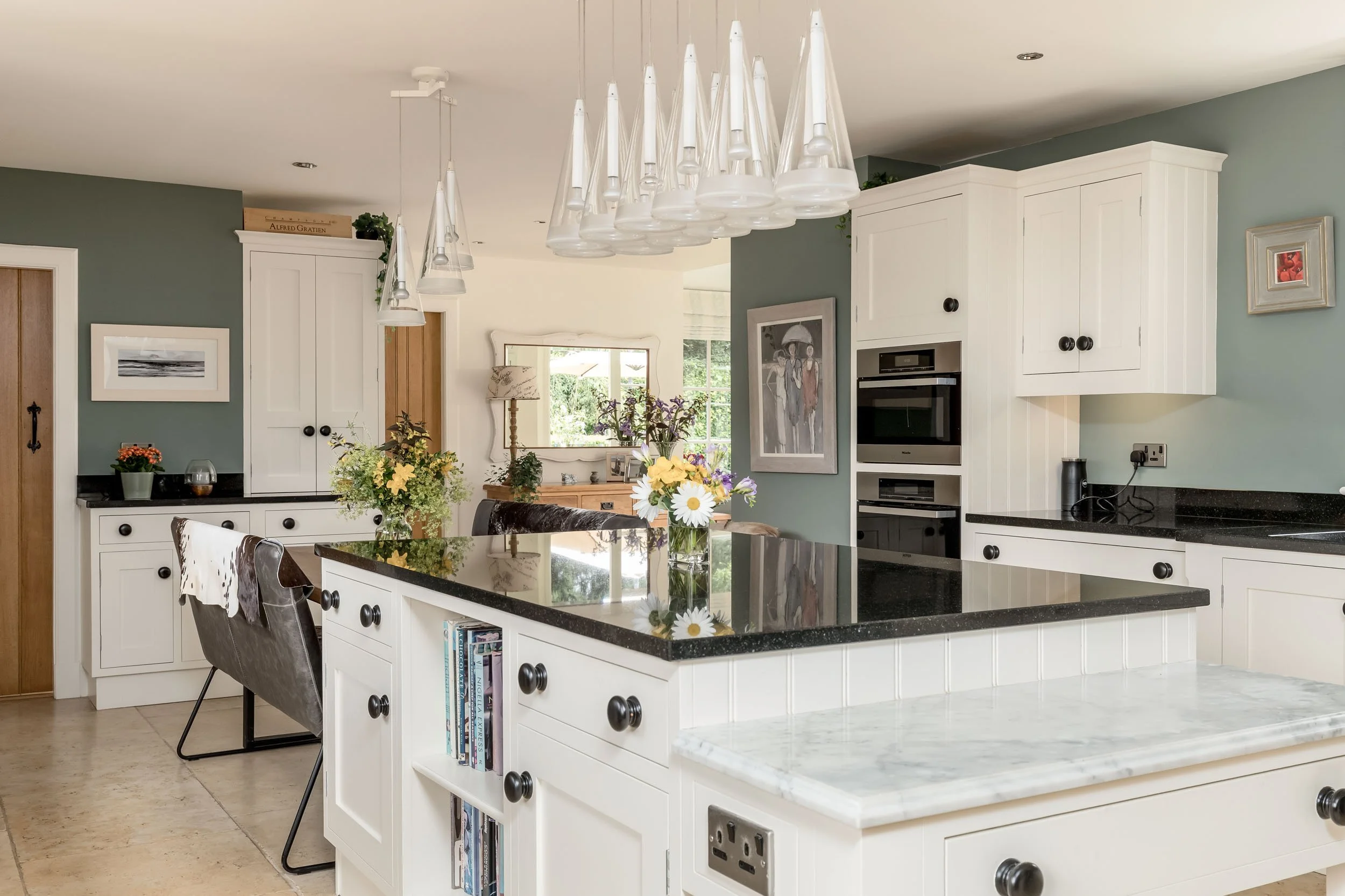 Contemporary kitchen with white cabinets, a black granite island, and a modern glass chandelier above.